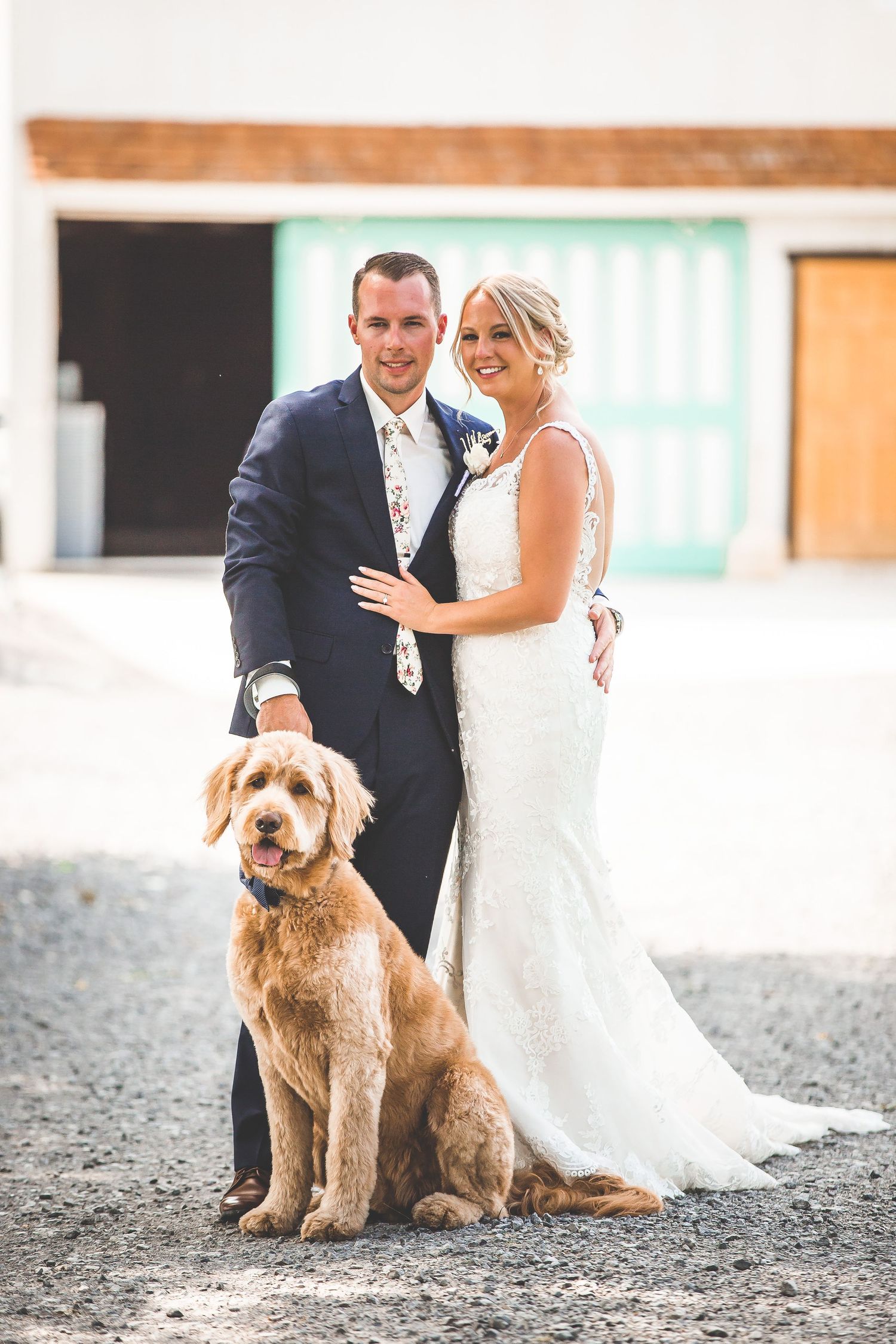 A couple in wedding attire poses with their golden doodle dog on their special day.