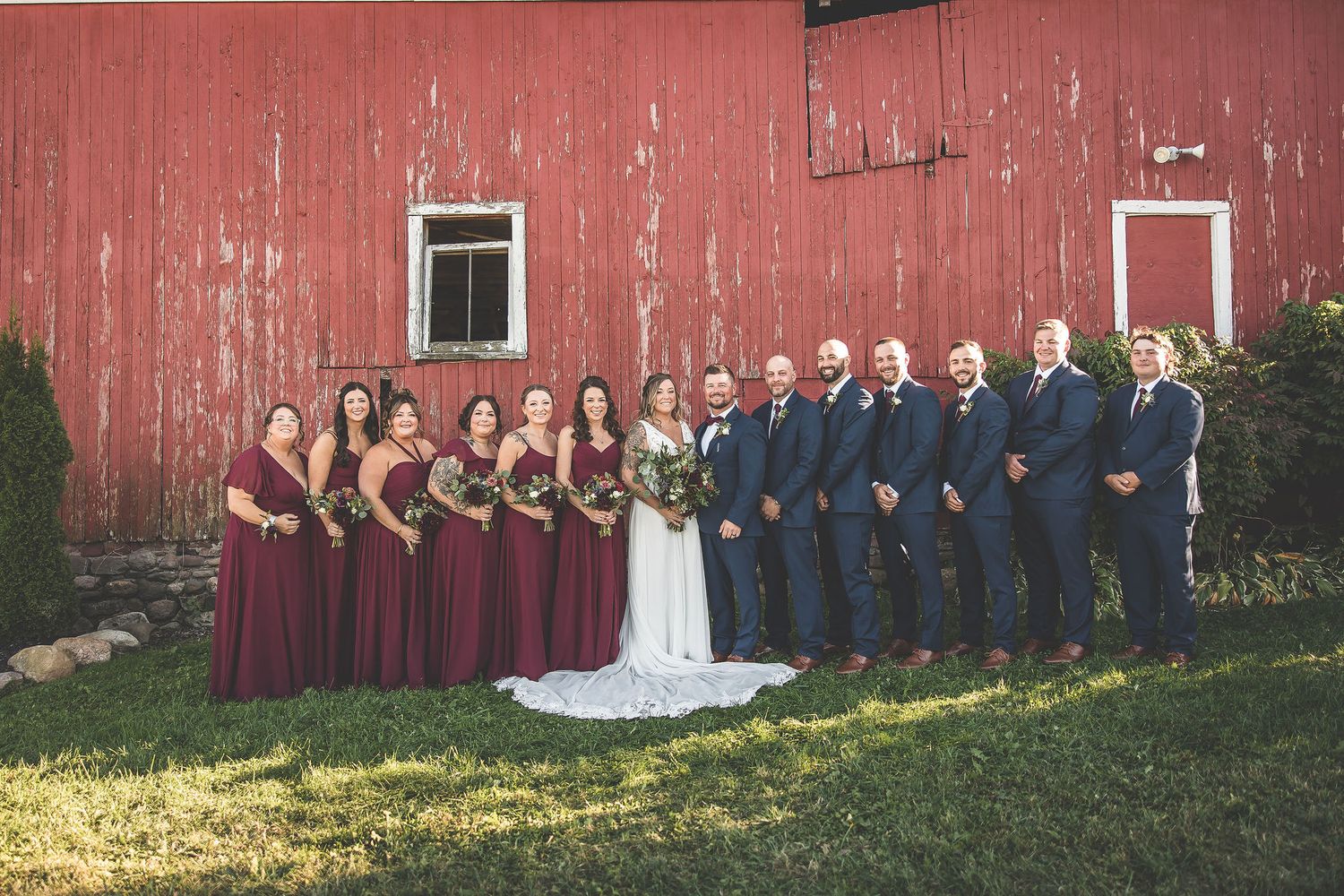 Panoramic shot of entire wedding party lined up along length of rustic red barn.