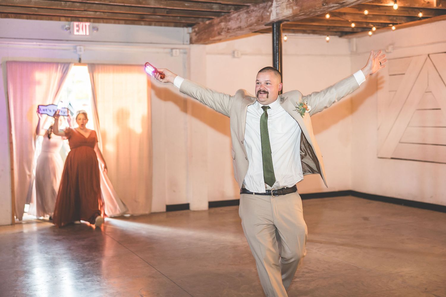 Wedding party dancing and celebrating in industrial venue with string lights.