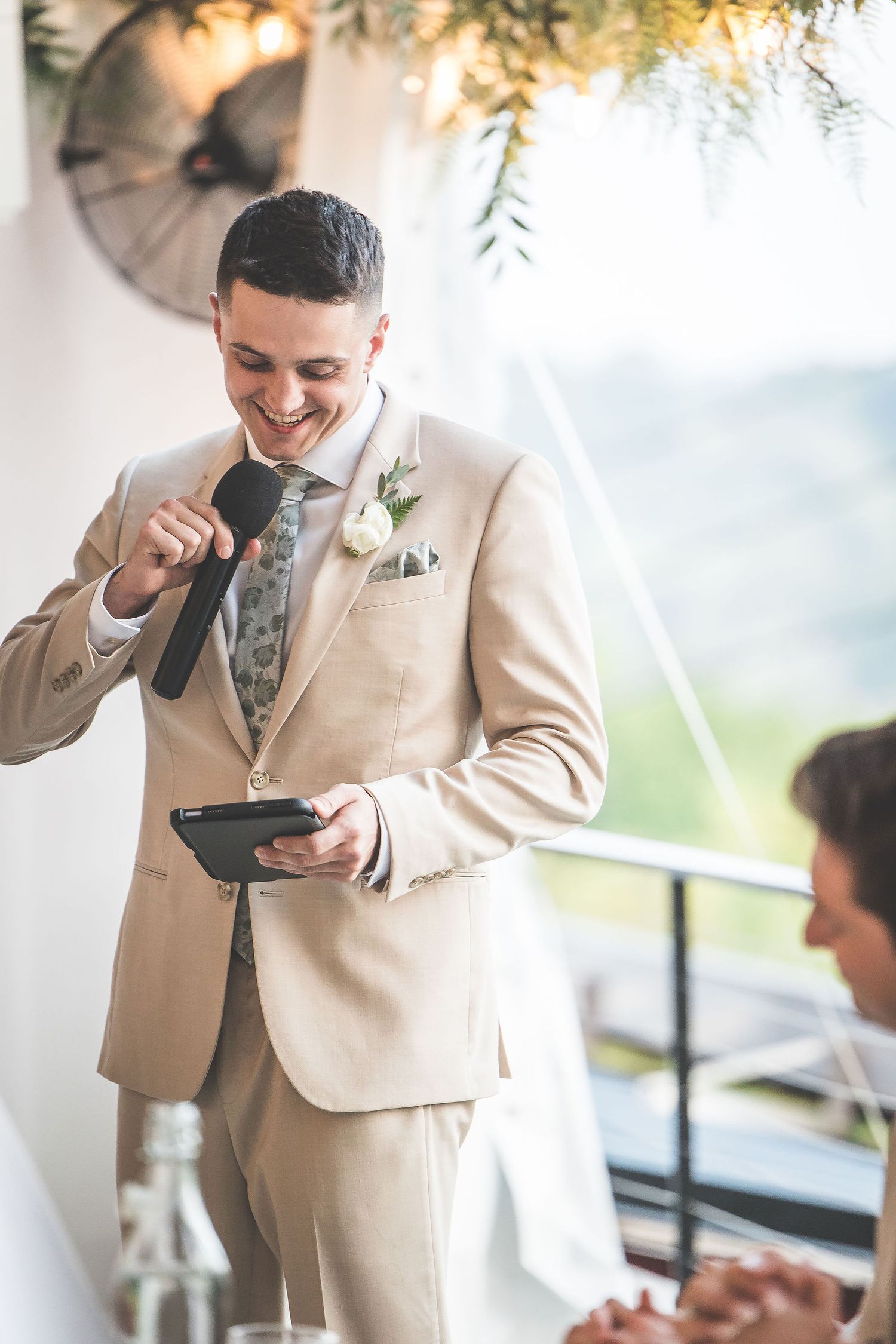 A person in a tan suit and tie gives an emotional speech during a wedding reception.