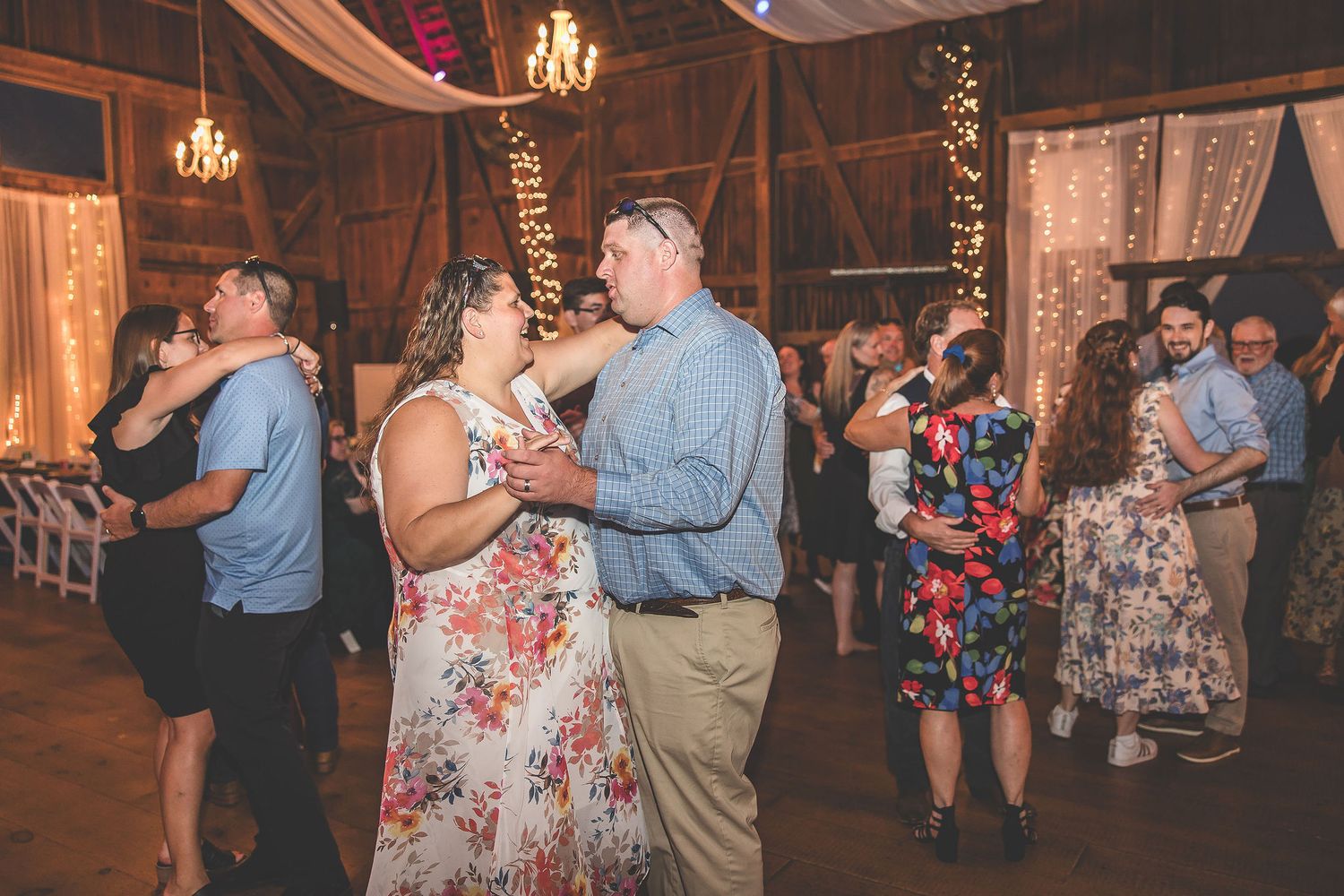 Wedding reception dance party in a rustic barn venue decorated with string lights and fabric draping.