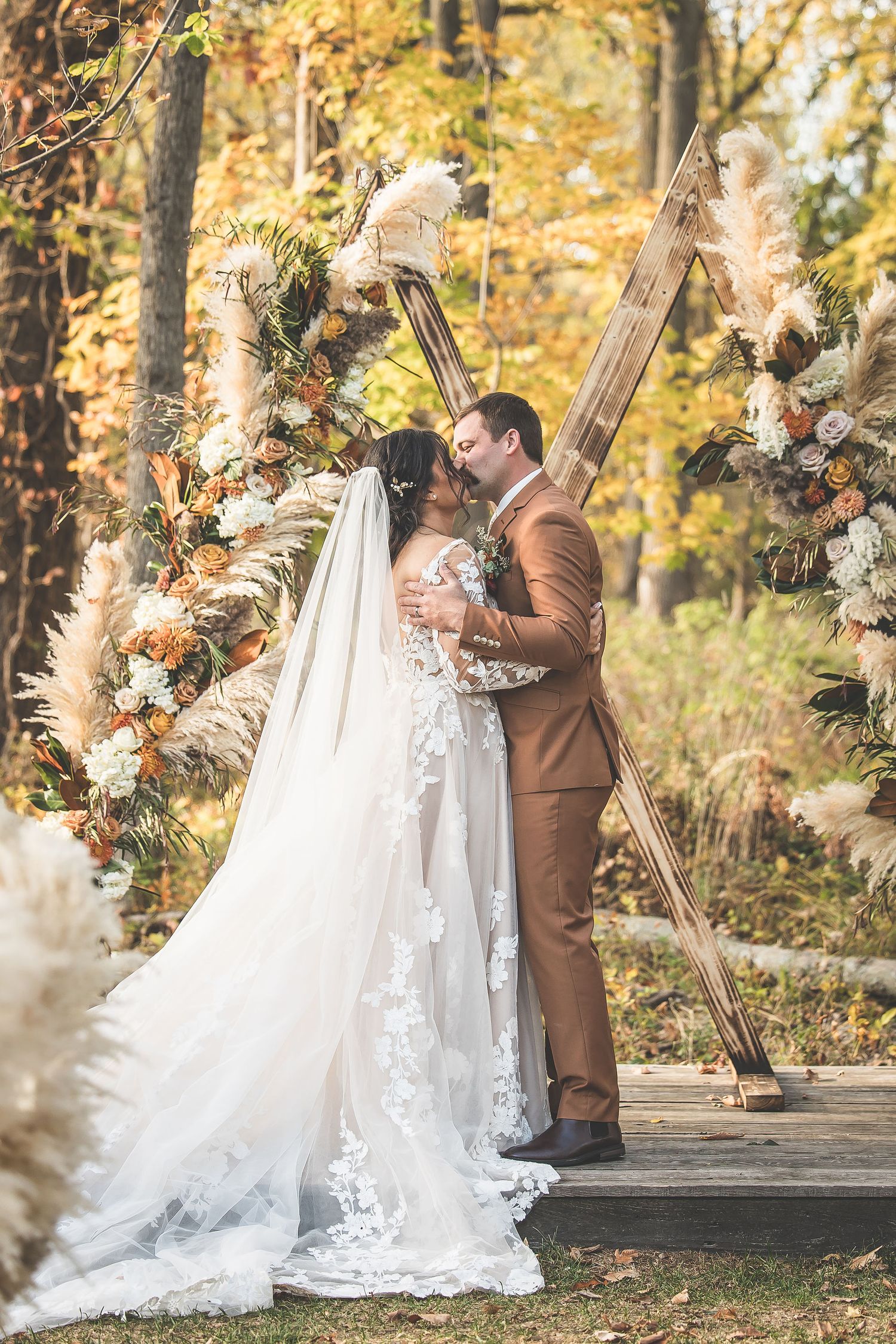 Wedding couple standing at rustic wooden altar decorated with autumn floral arrangements.