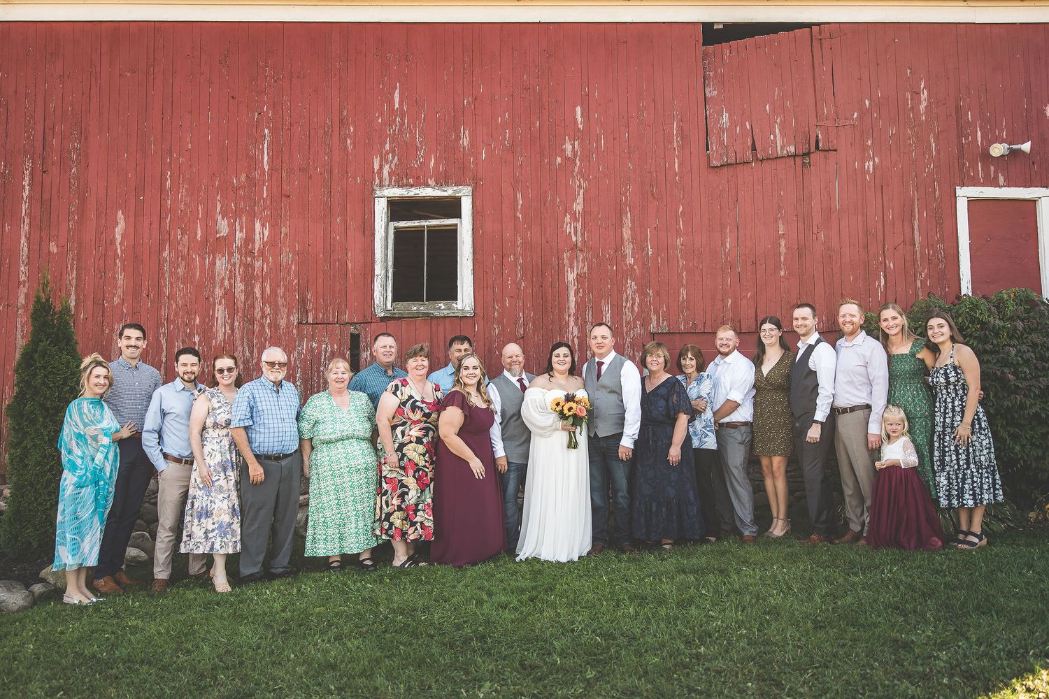 Large group wedding photo with guests lined up against a red barn exterior.