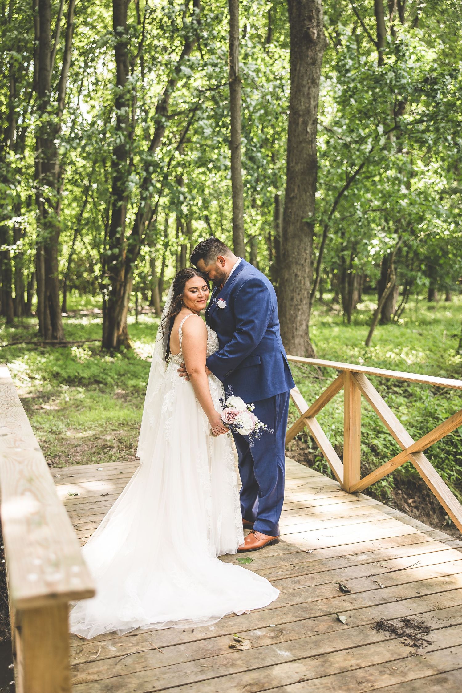 A romantic wedding photoshoot on a wooden bridge surrounded by lush green forest.