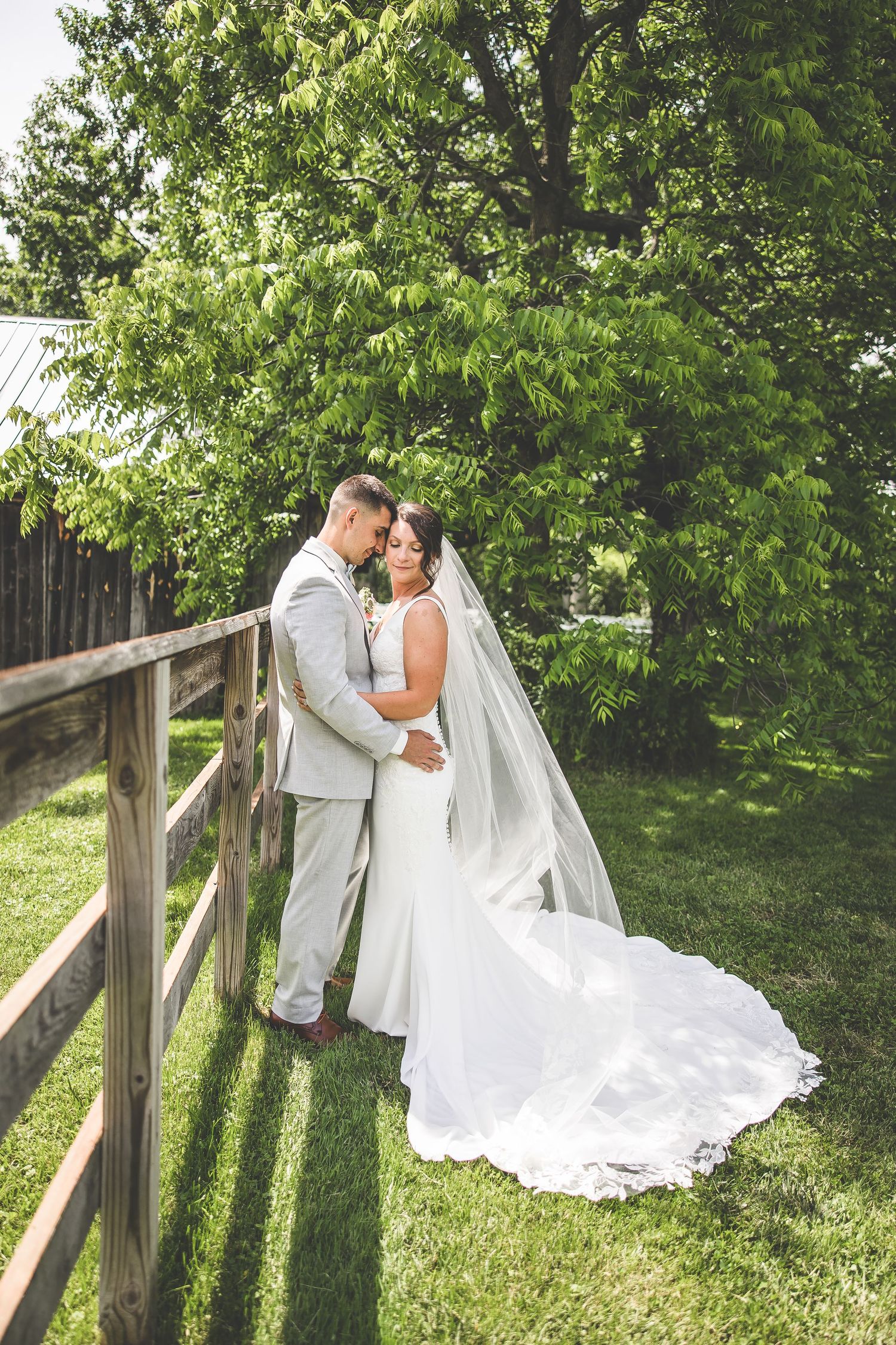 Romantic wedding photos by rustic fence with flowing white dress and green background.