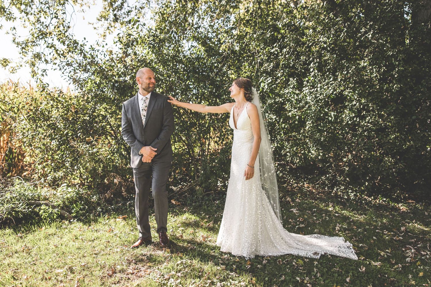 A touching first look reveal between a couple in formal wedding attire surrounded by lush greenery.