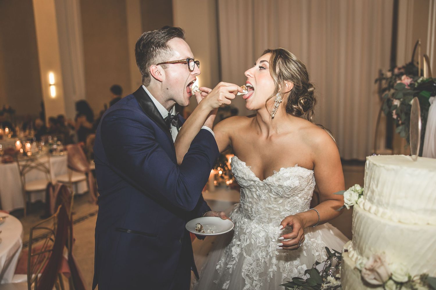 Traditional cake feeding moment during wedding reception with white tiered cake.
