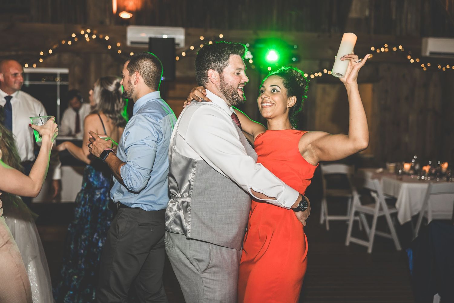 Energetic wedding reception with guests dancing under colorful lights in a barn setting.