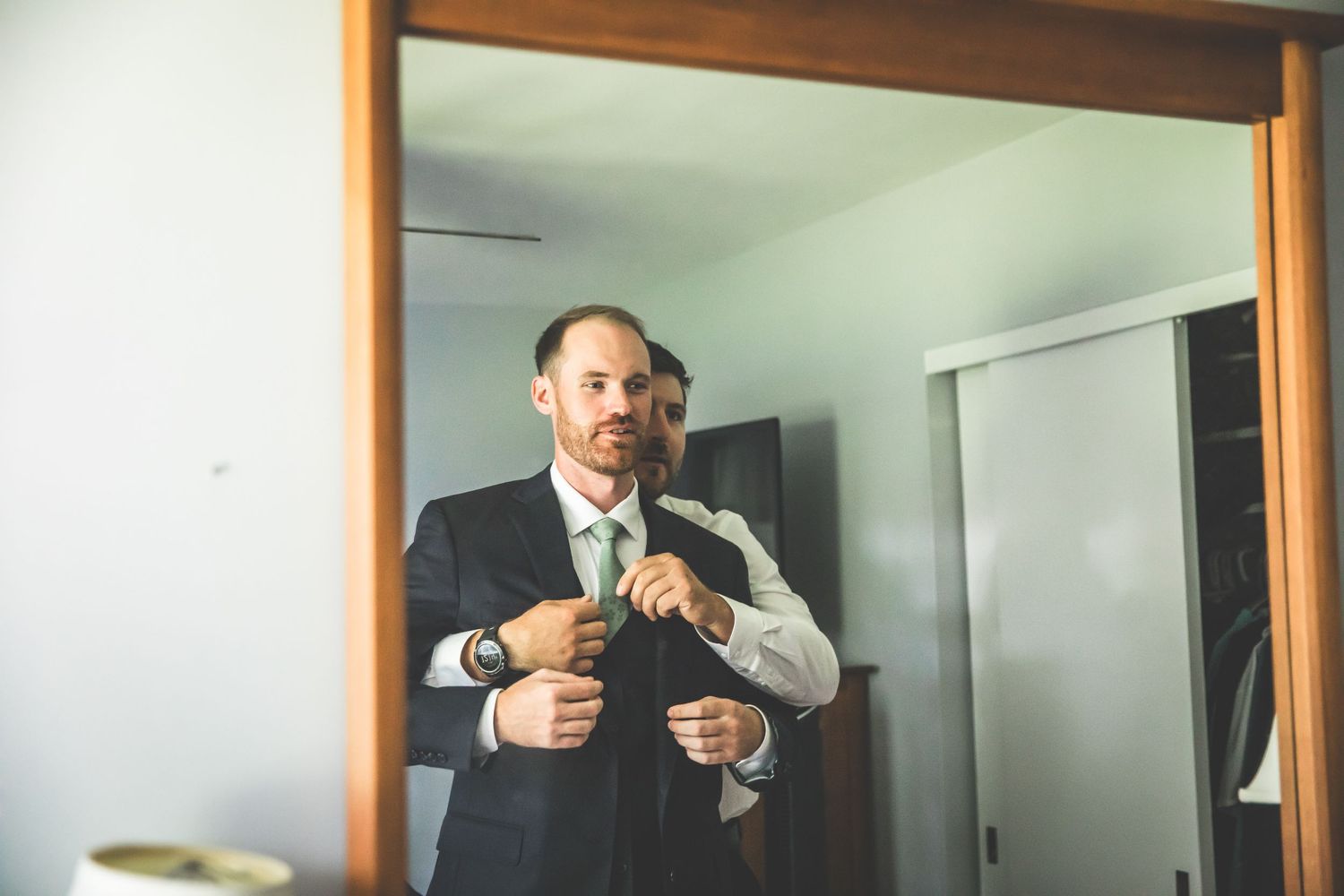 Men in formal attire getting ready in a minimalist room with wooden trim.