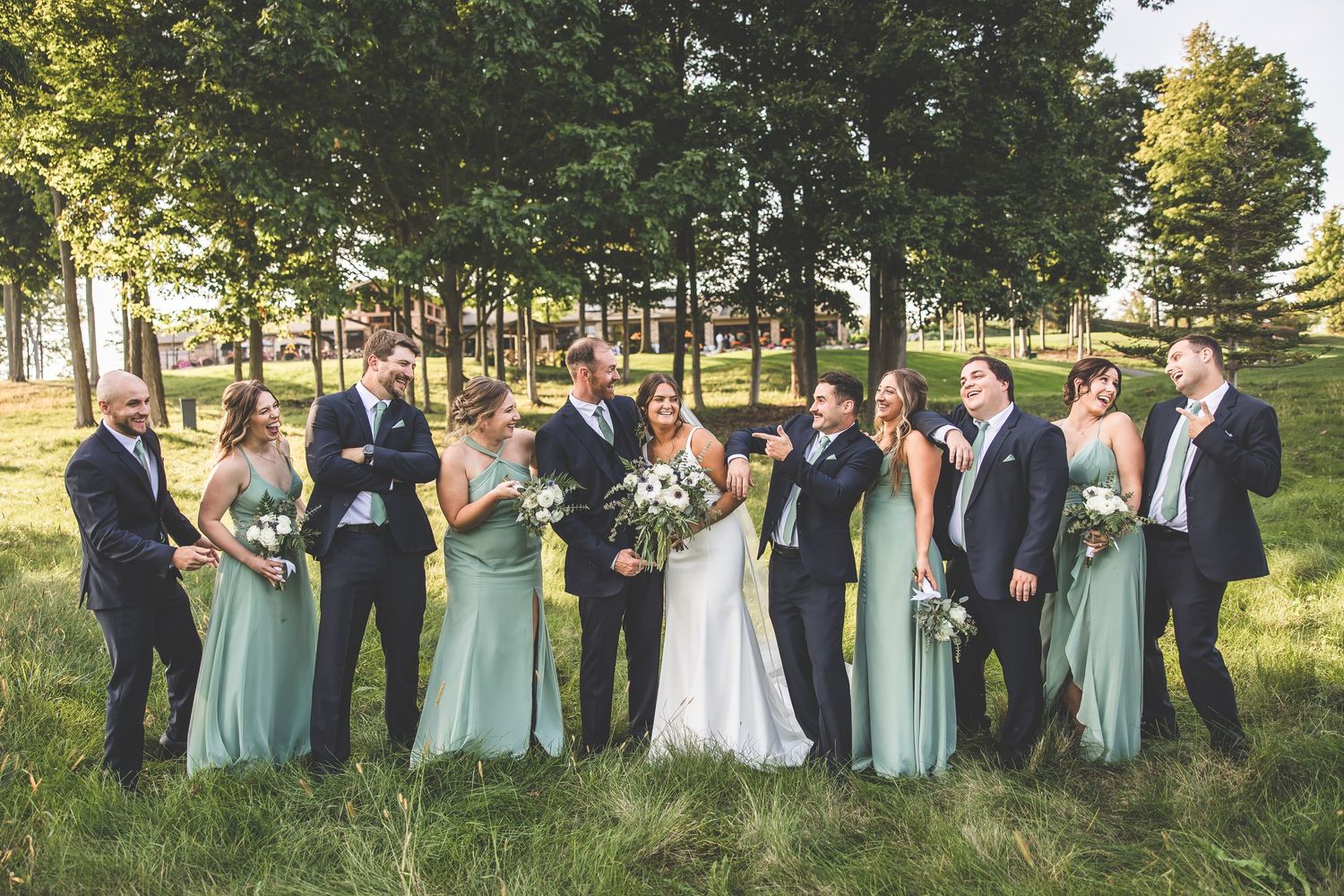 Wedding party laughing and socializing in casual group photo outdoors.