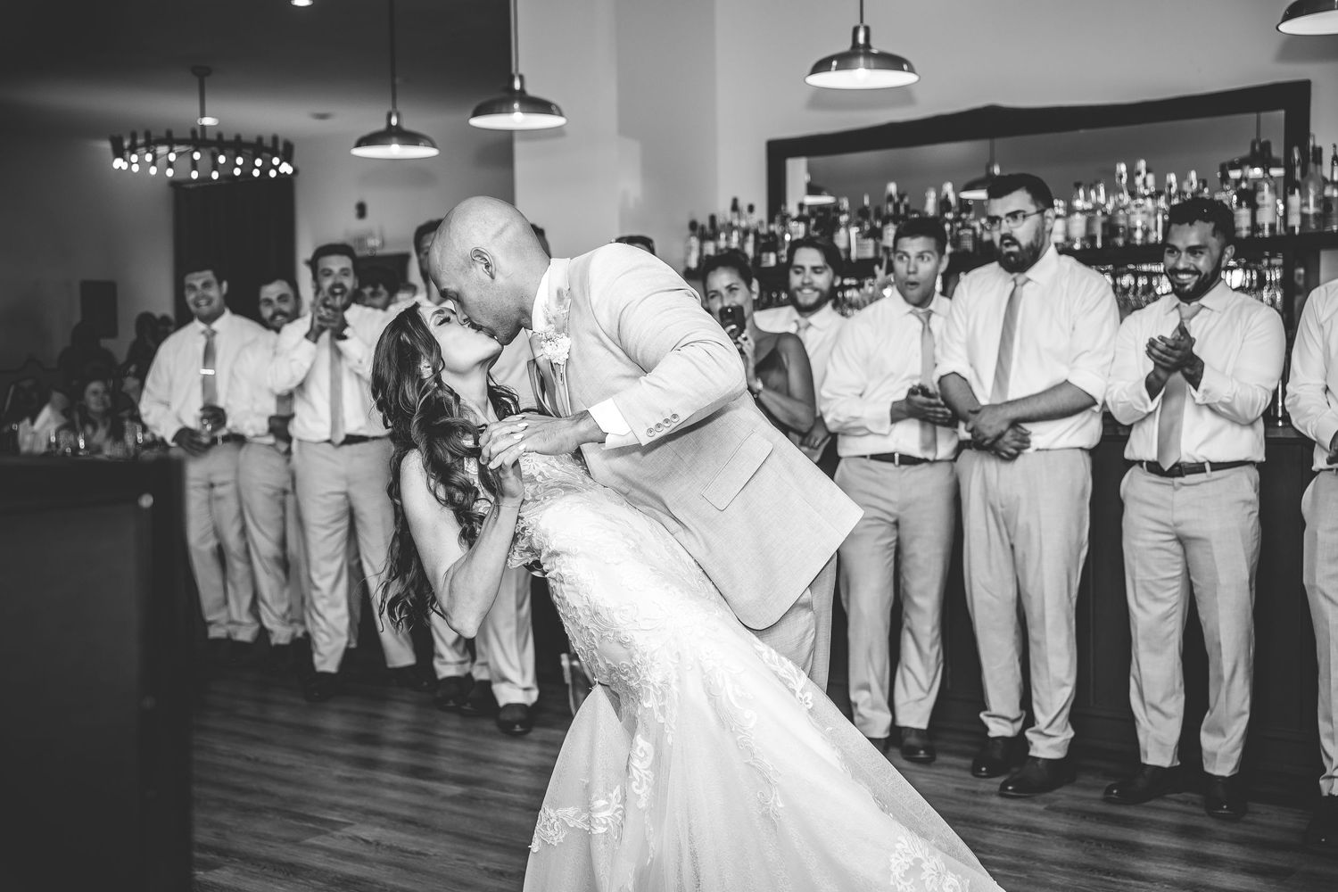Wedding reception in monochrome showing guests dancing under industrial pendant lighting.