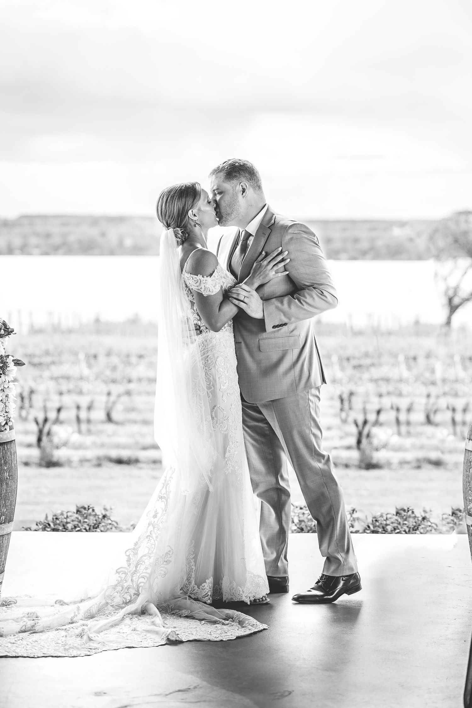 Black and white romantic portrait of newlyweds embracing with vineyard in background.