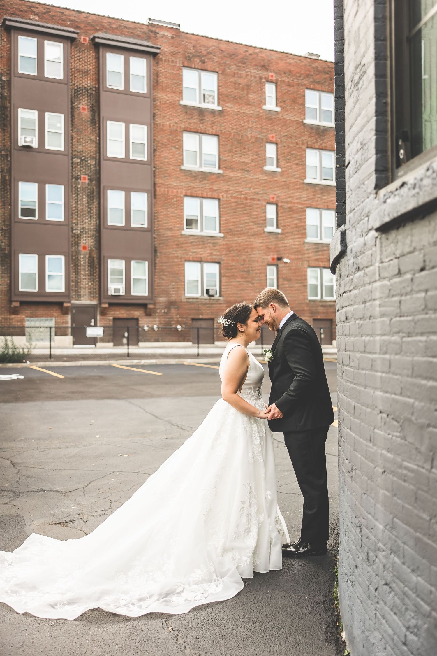 Wedding couple posing against a rustic brick wall backdrop in an urban setting.