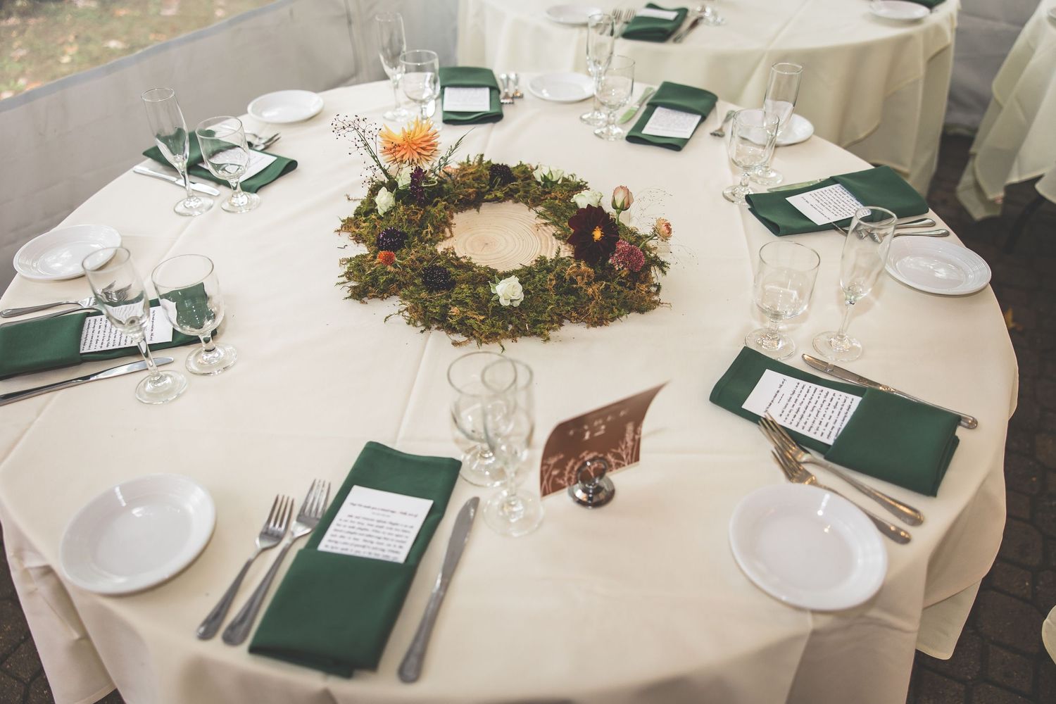 Elegant round table setting with a natural moss wreath centerpiece and green napkins.
