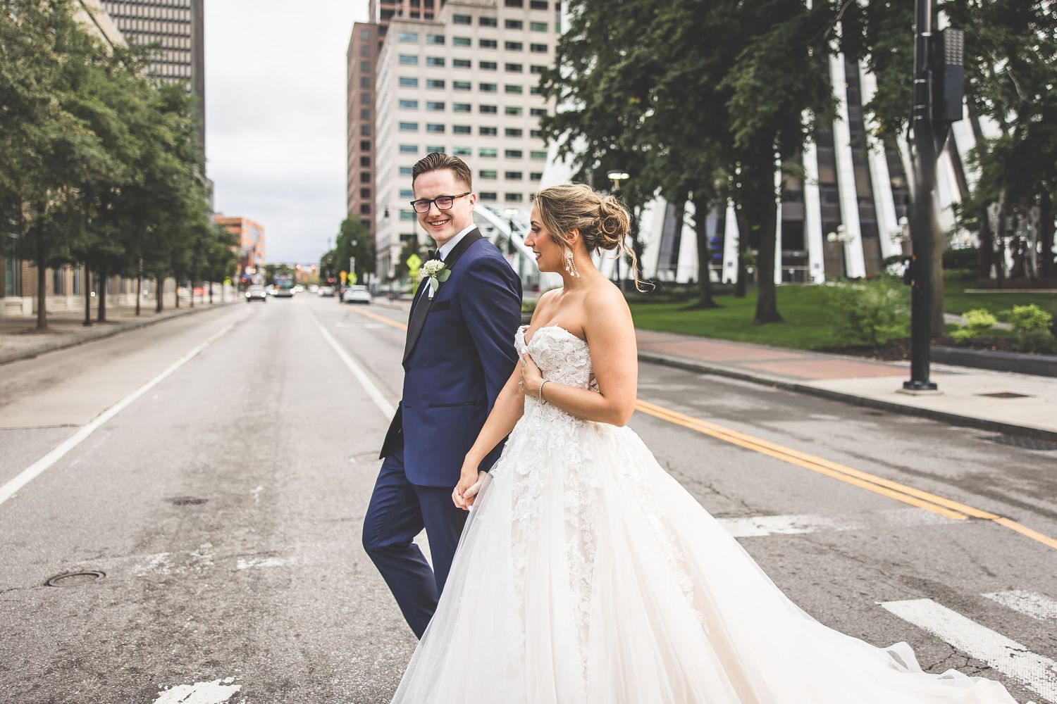 Newlyweds dance and twirl on empty city street with buildings in background.