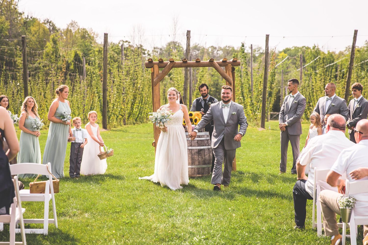 Panoramic view of outdoor wedding ceremony setup with white chairs in vineyard setting.