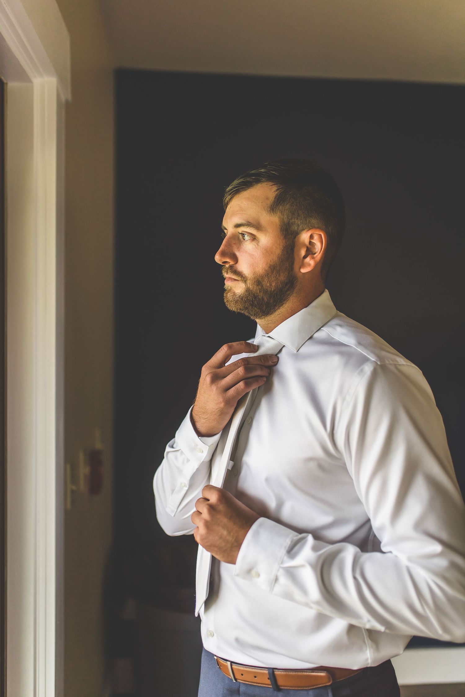 Man in white dress shirt adjusts his collar while getting ready.