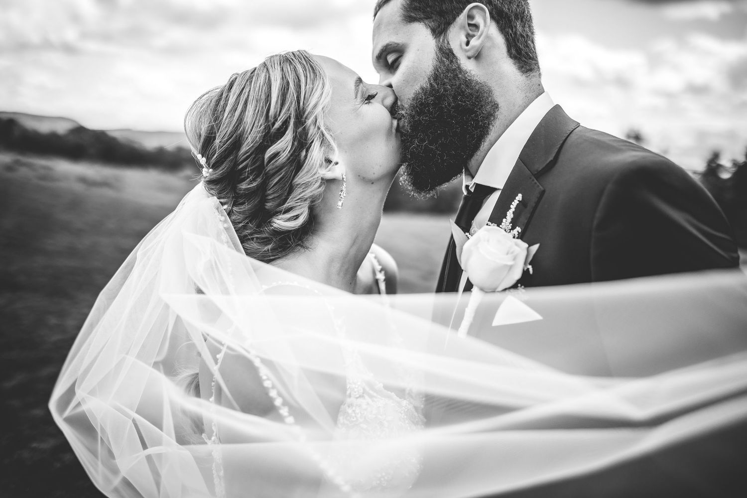 Black and white romantic wedding veil shot with couple kissing outdoors.