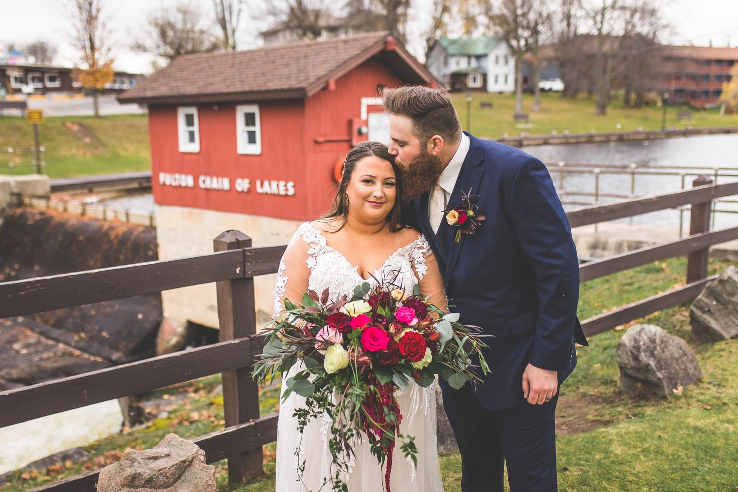 Autumn wedding photos taken outside red barn with fall foliage in background.