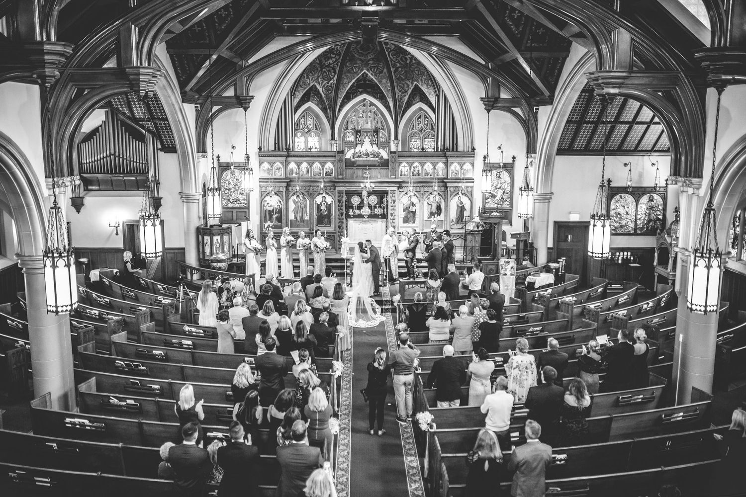 Panoramic black and white view of church pews filled with wedding guests.