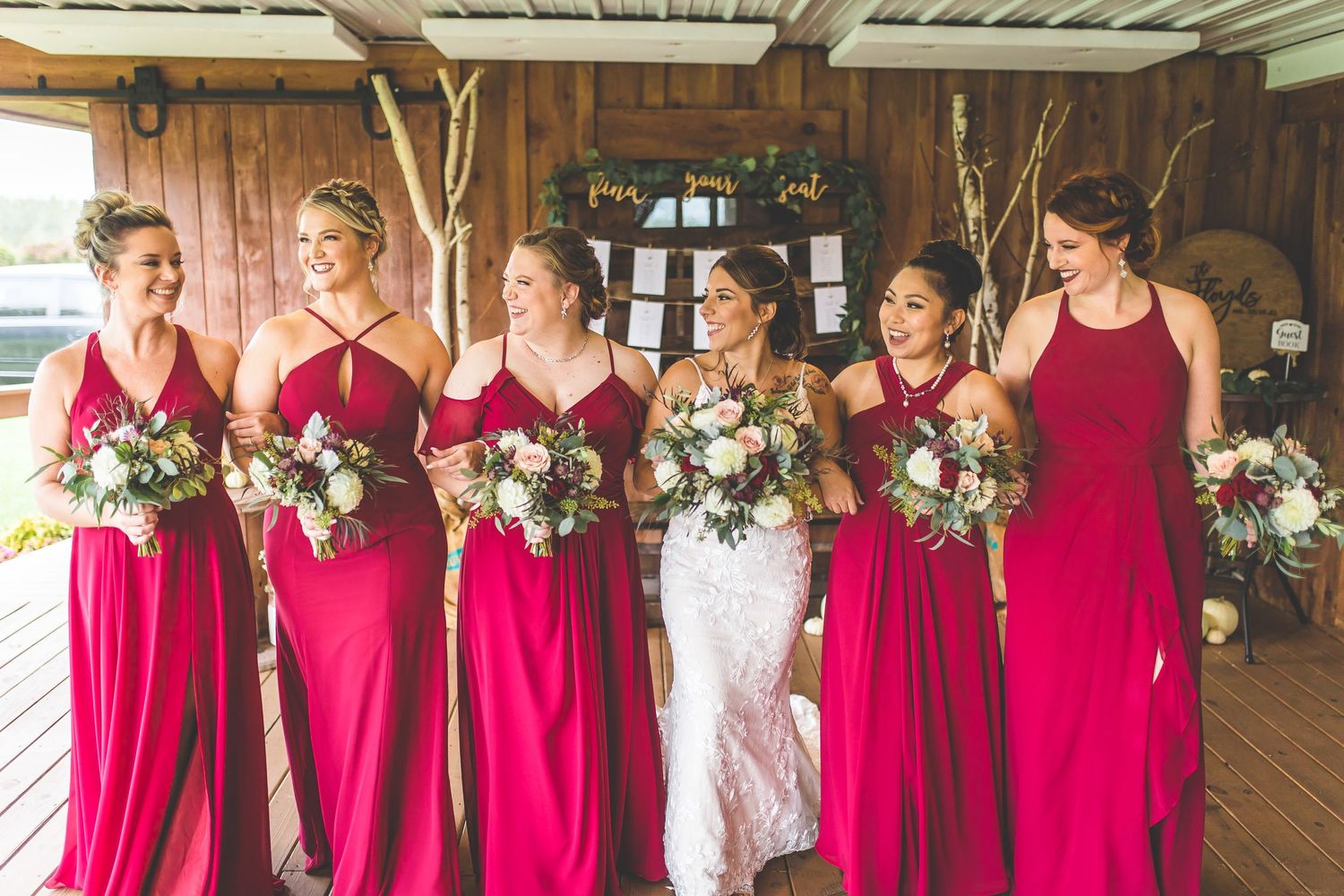Wedding party lineup in a rustic barn setting with bridesmaids in red dresses and floral bouquets.