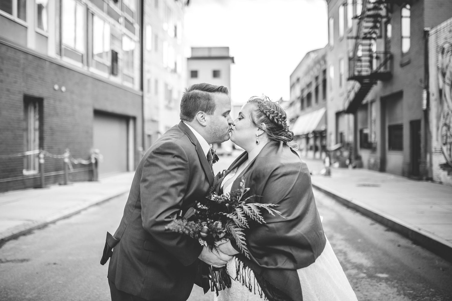 Black and white photo of newlyweds sharing an intimate moment on a city street.