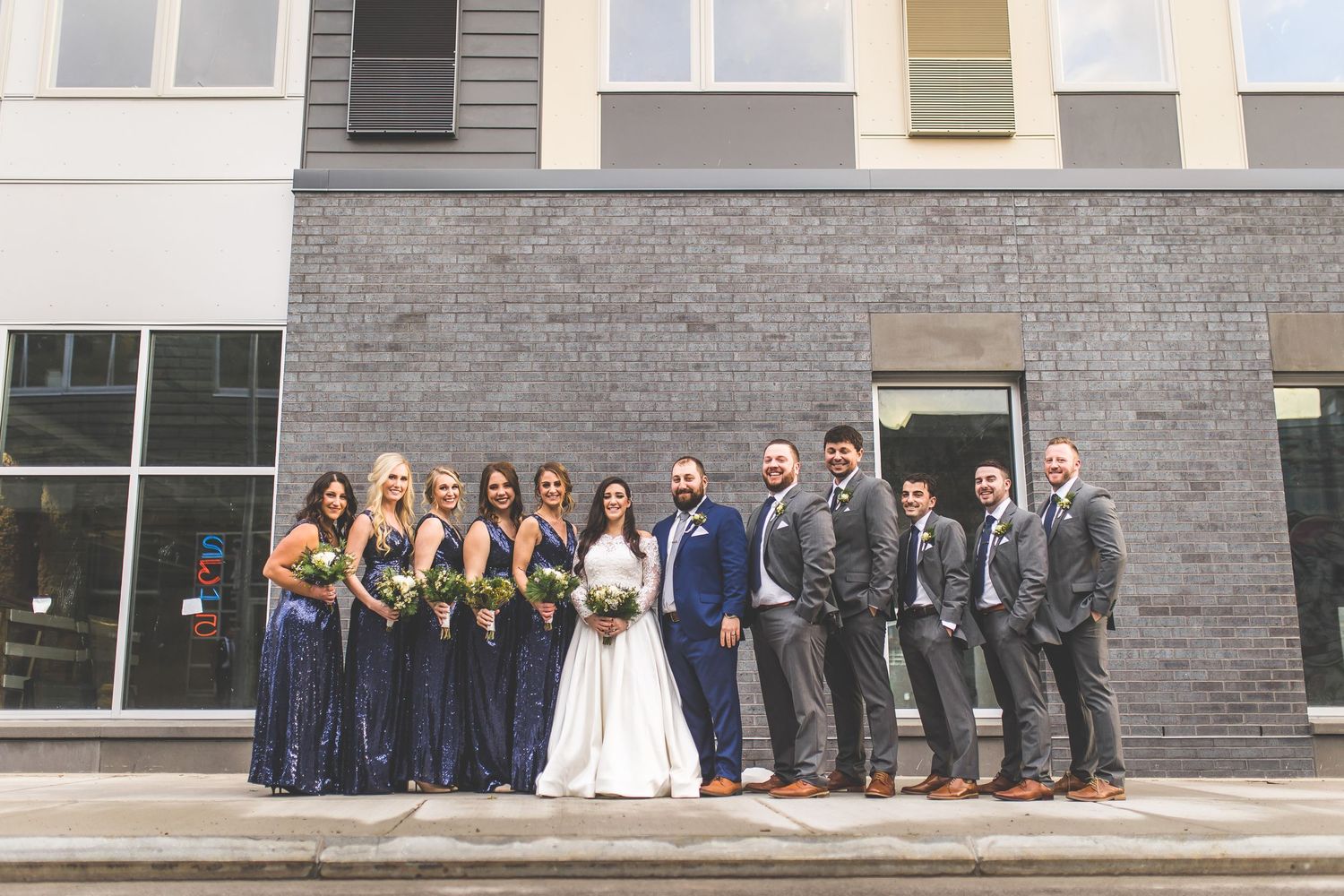 Wedding party lined up outside modern building with navy and gray color scheme.