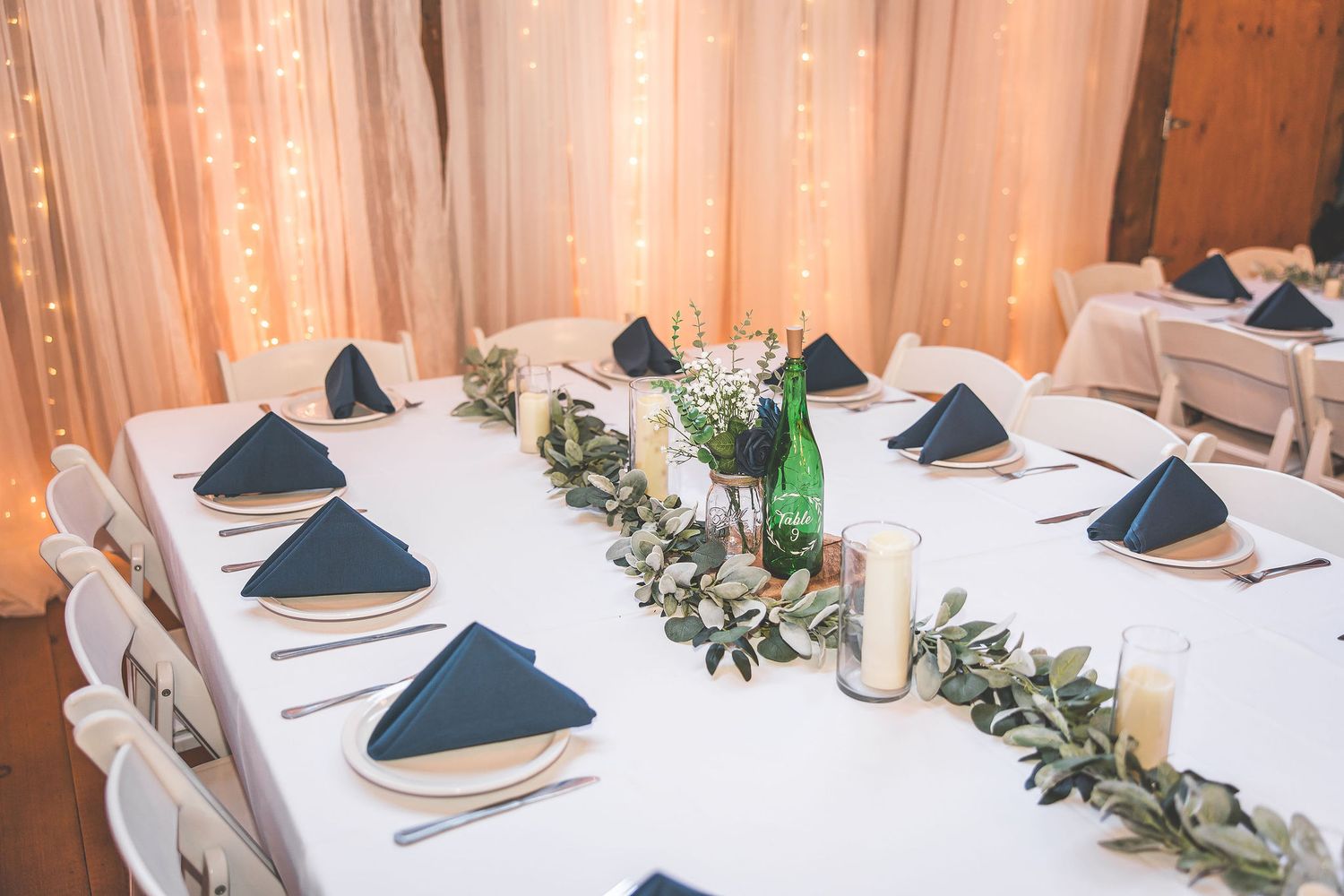 Wedding reception table settings with navy blue napkins and greenery garland centerpieces.