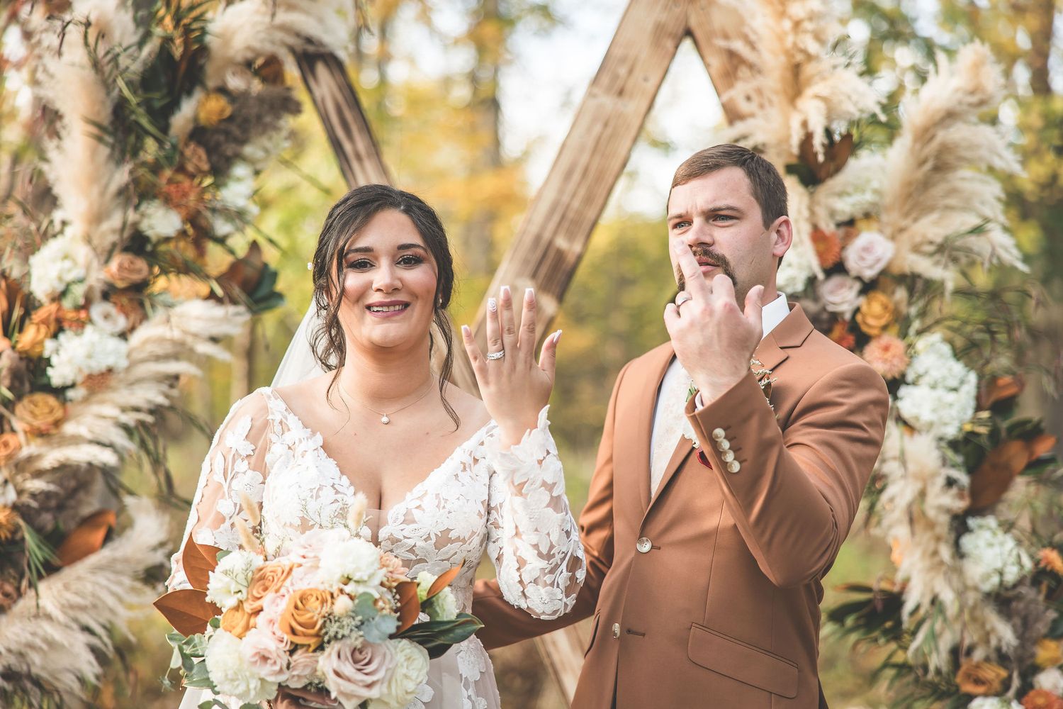 Couple celebrating during outdoor autumn wedding ceremony with decorative arch.