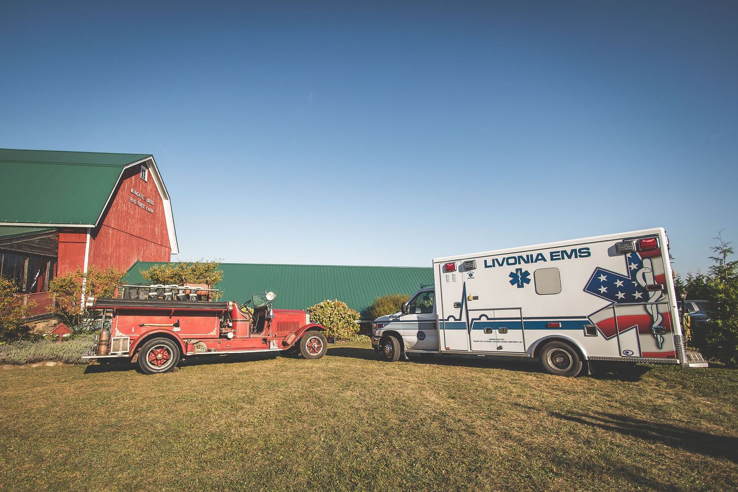 Line of emergency and service vehicles parked on a hill near a red barn.
