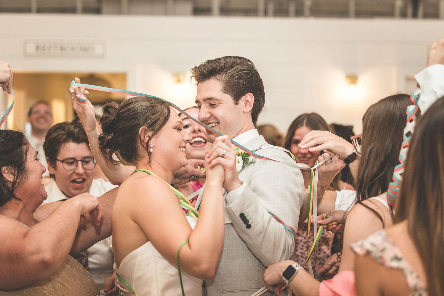 Wedding guests dance and embrace during a lively celebration in an indoor reception hall.