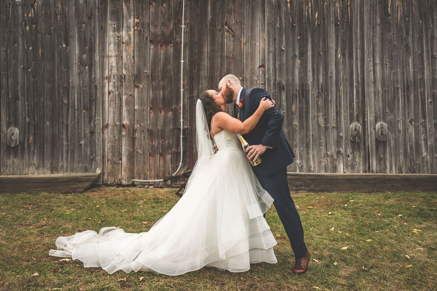 Couple shares romantic dance moves against rustic wooden barn background.