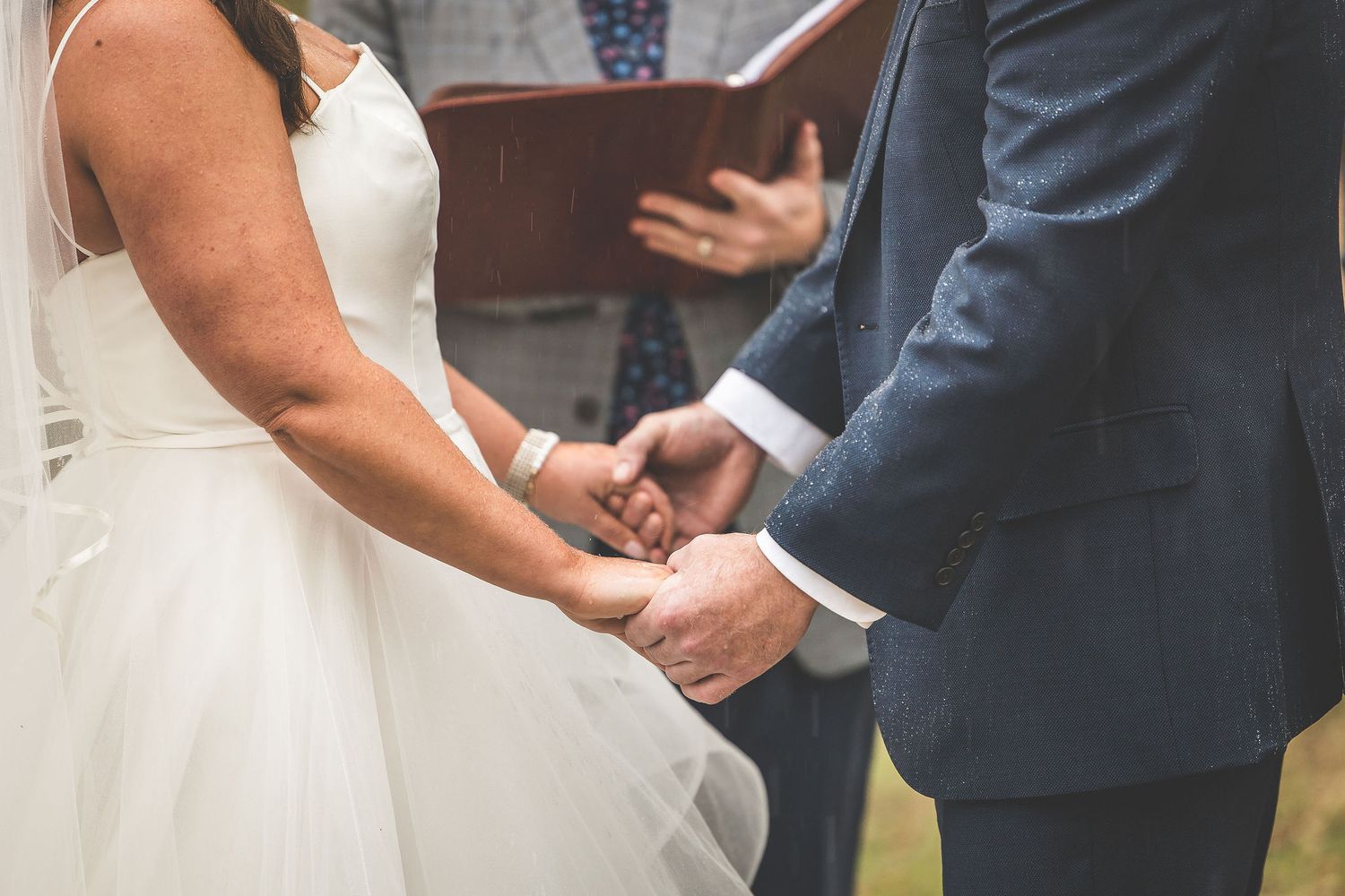 Close up of couple holding hands during outdoor wedding ceremony with officiant.