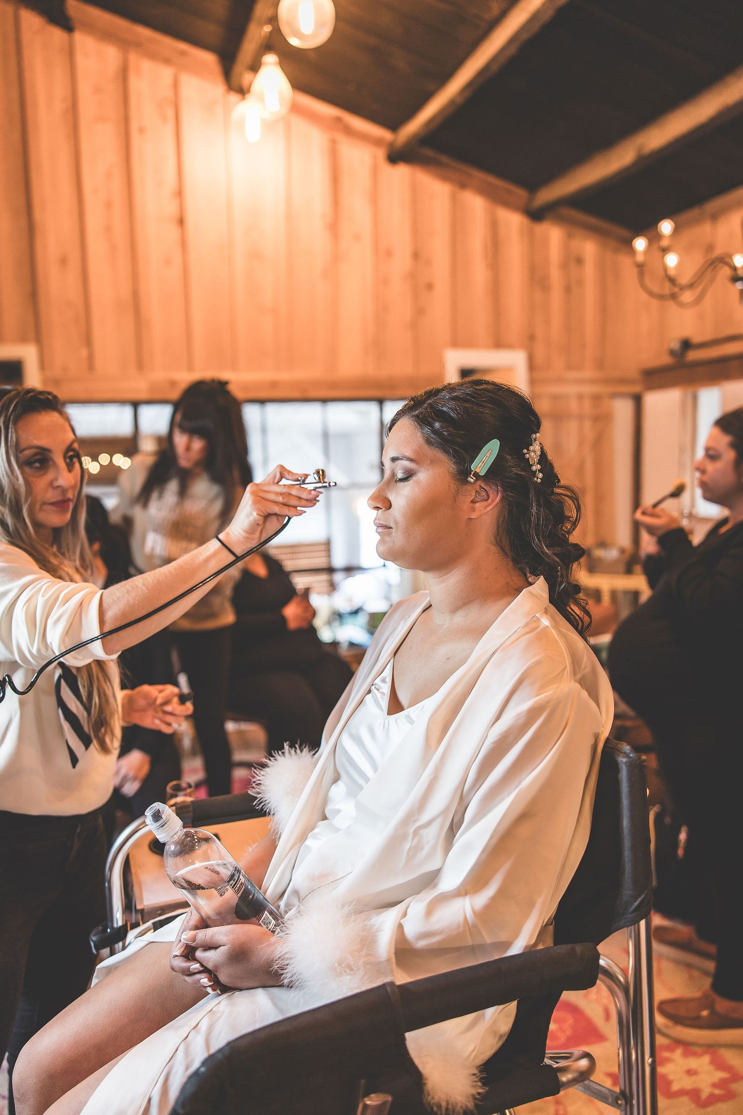 Wedding preparations in a rustic wooden venue as makeup is being applied in warm lighting.