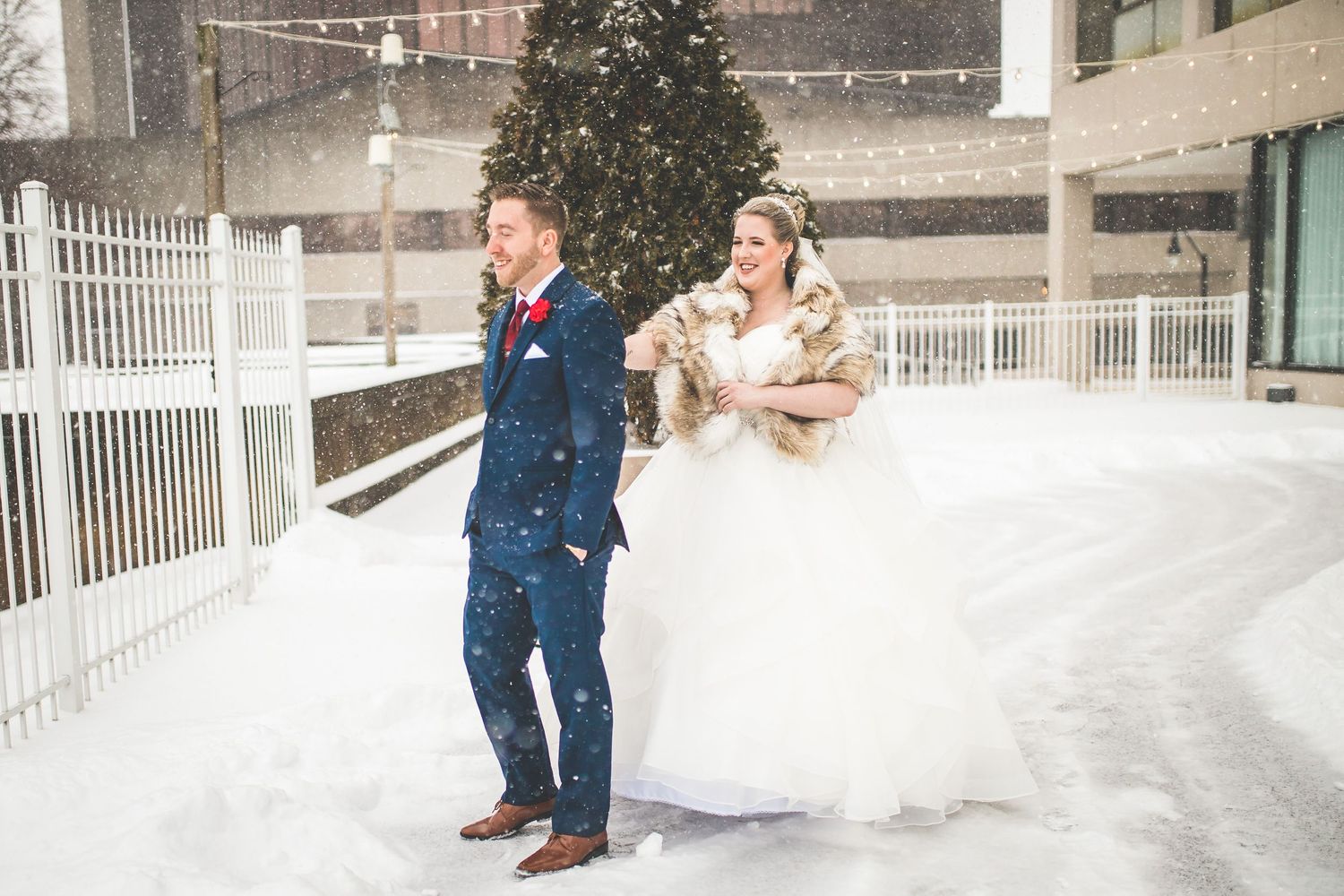 Snowy winter wedding scene with white fencing and string lights.