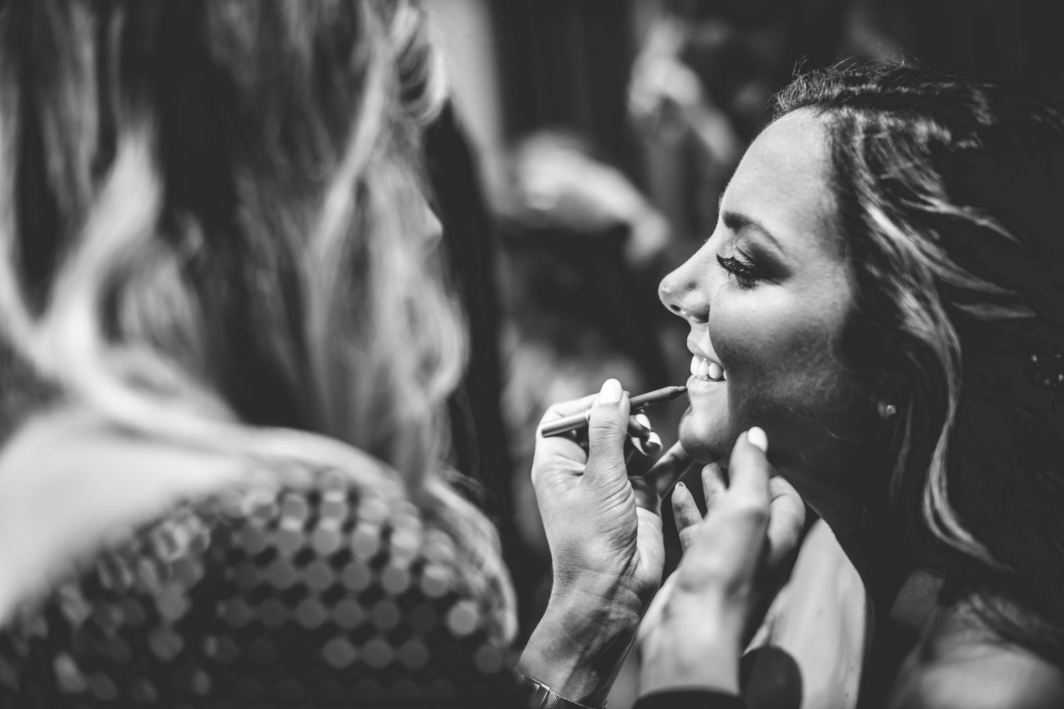Black and white photo of someone having makeup applied before the wedding.