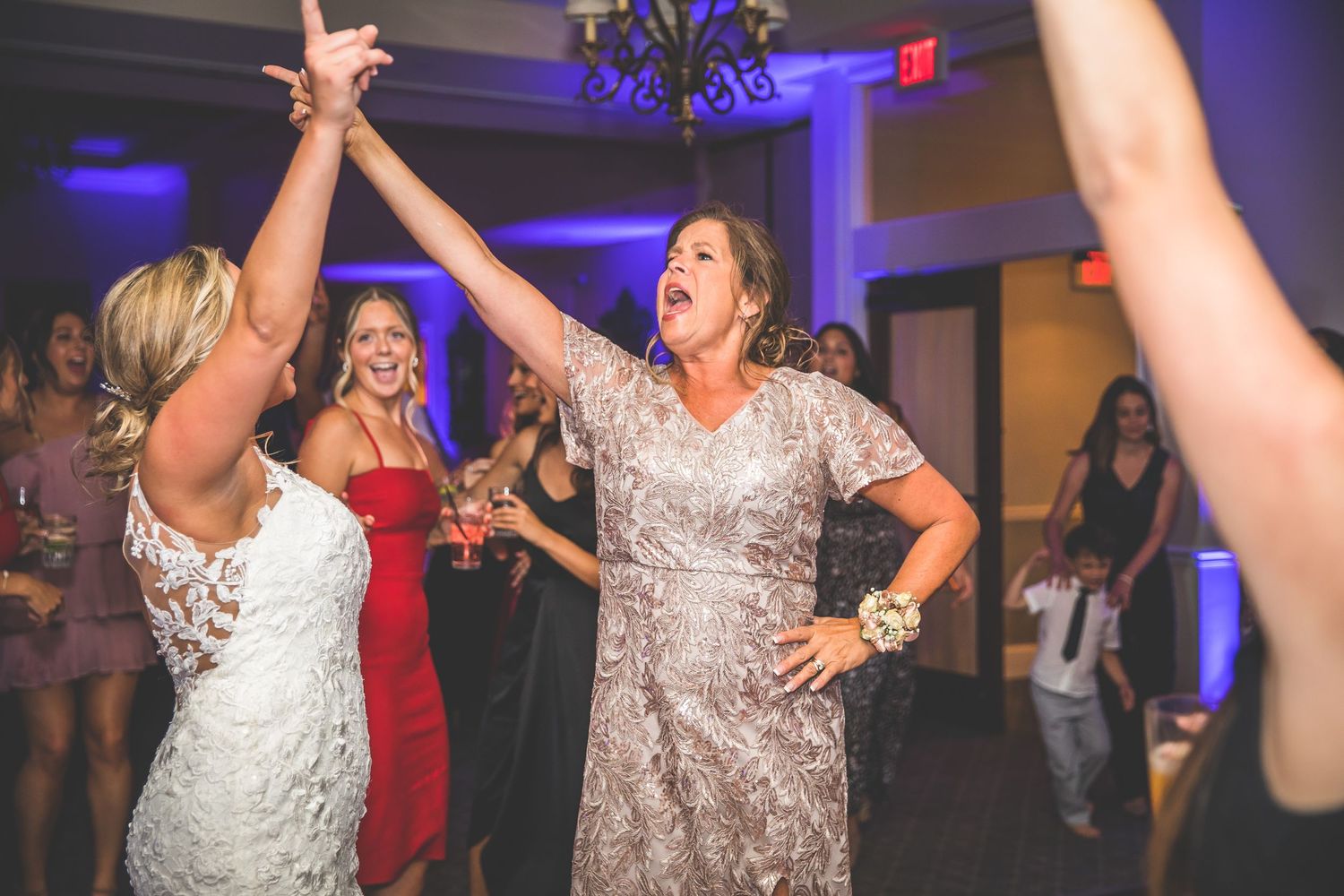 Wedding guests dancing enthusiastically at a reception with blue uplighting and festive atmosphere.
