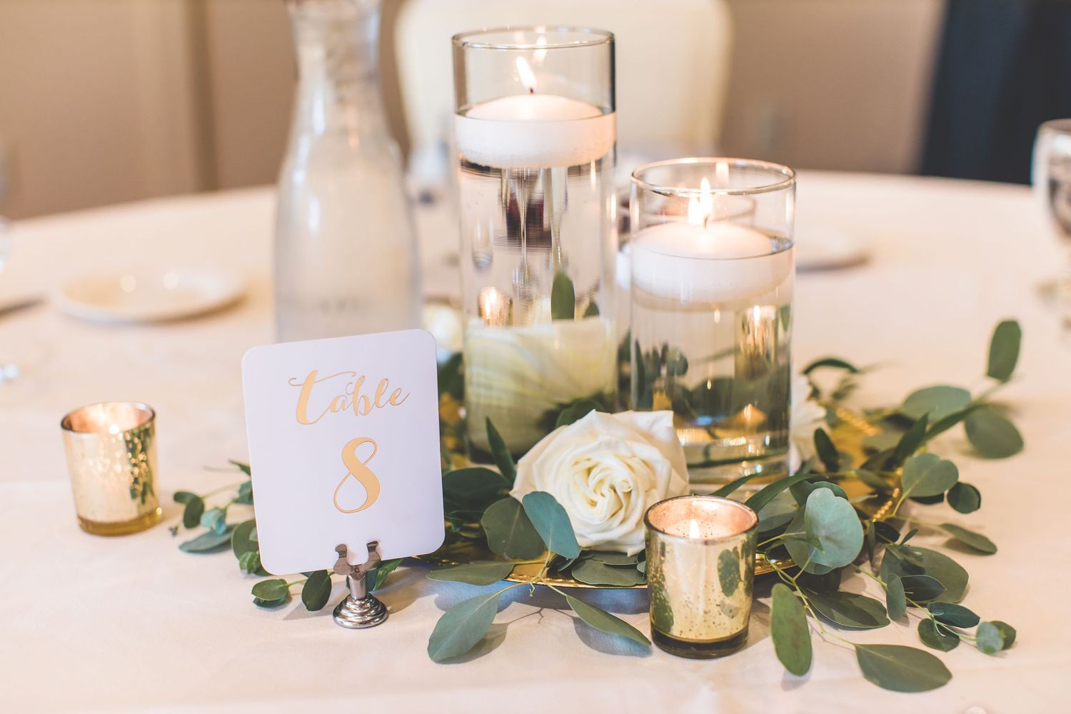 Elegant wedding table decor with white candles and eucalyptus greenery on white tablecloth.