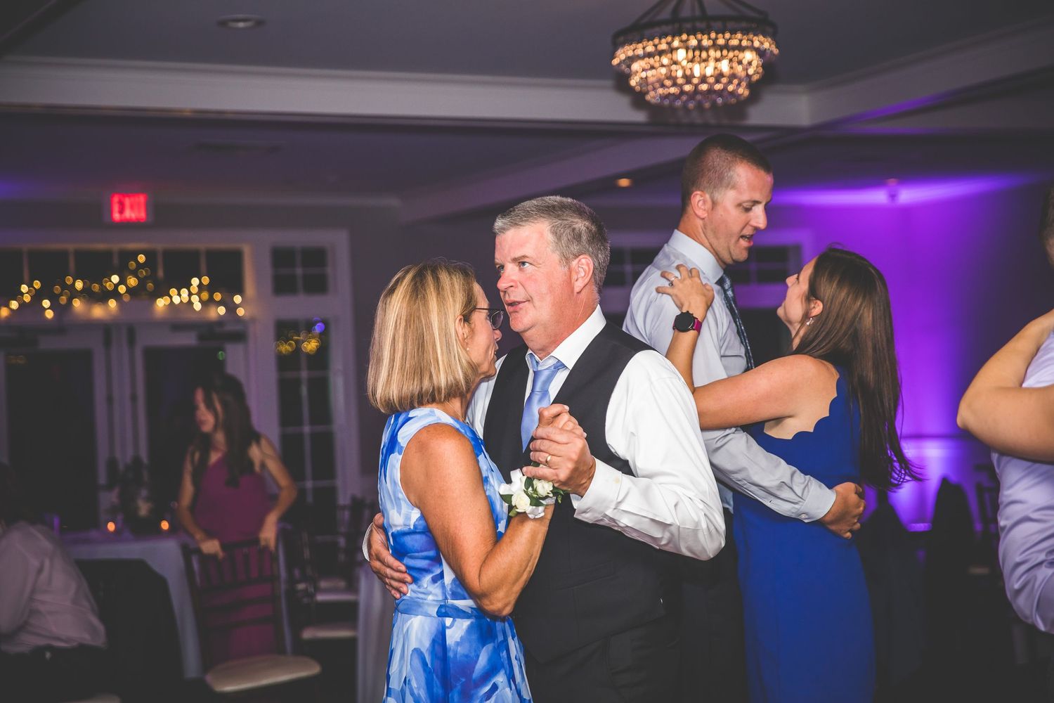 Couples dancing at an elegant wedding reception with purple uplighting and crystal chandeliers.