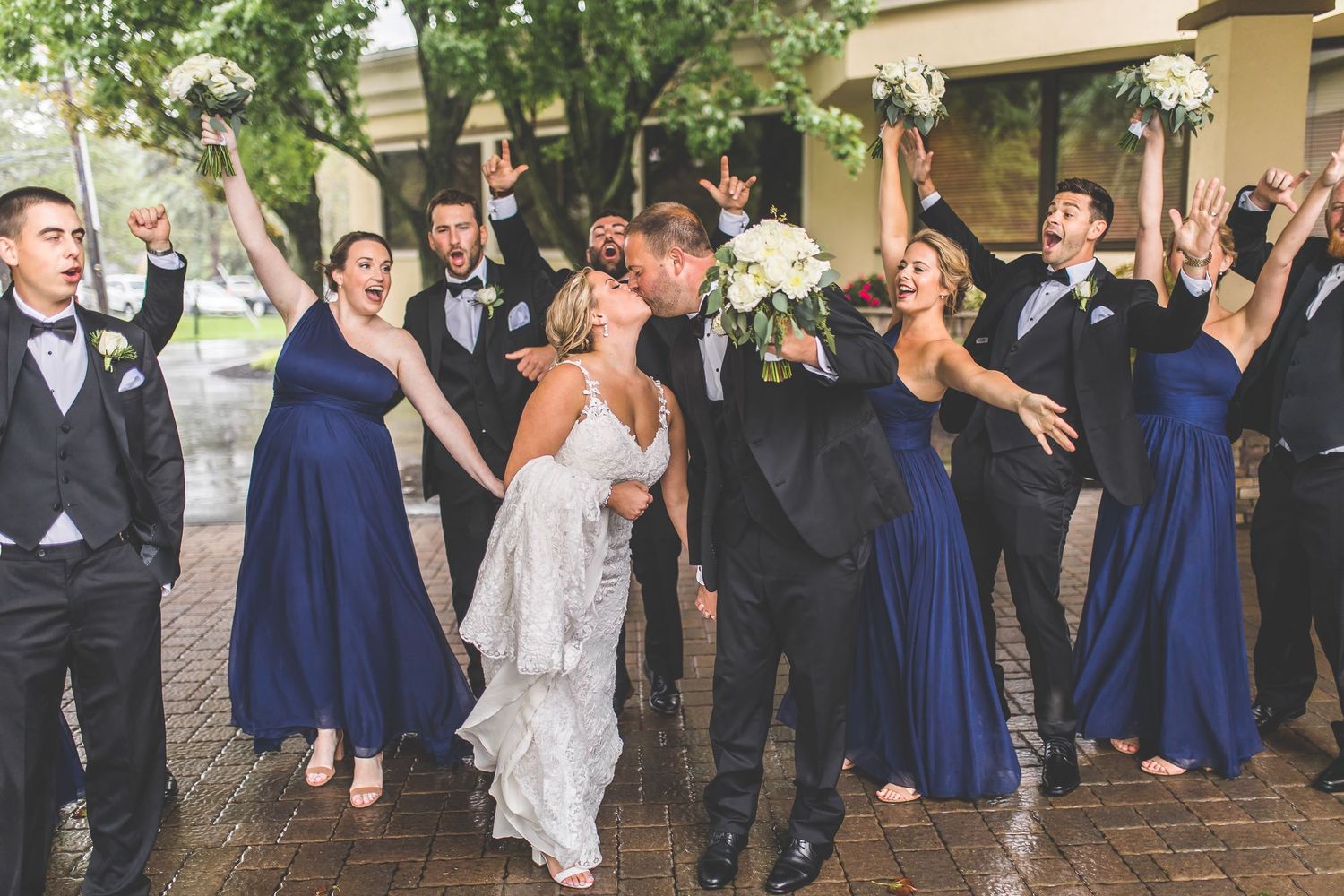 Large wedding party in navy and black attire poses playfully outdoors.