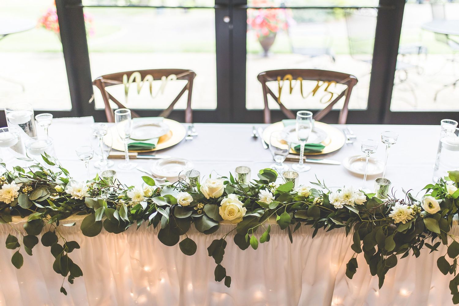 Elegant wedding table setting with greenery garland and cross-back chairs.
