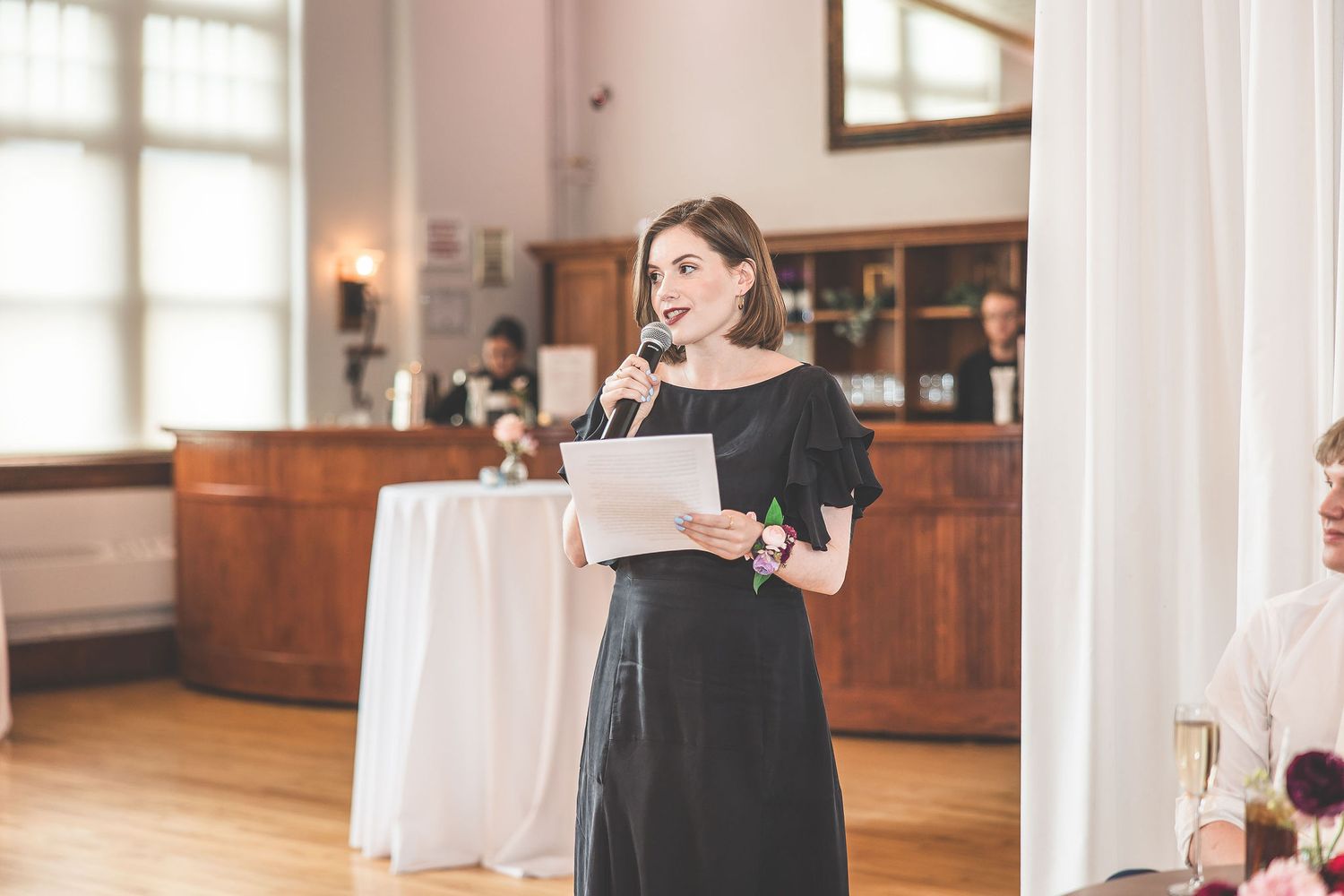 Elegant wedding reception venue with hardwood floors and white drapes features round dining tables.