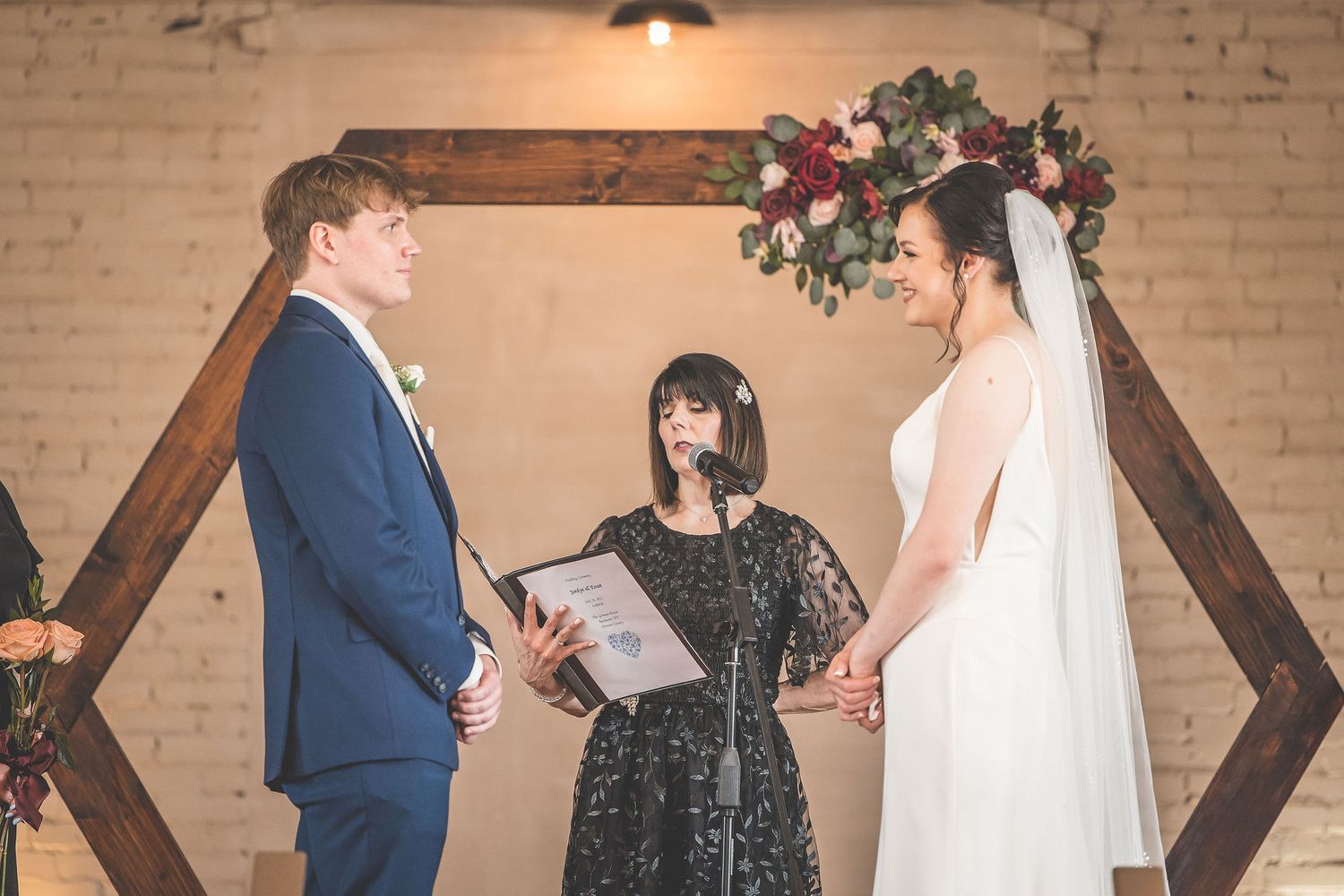 Wedding ceremony setup against exposed brick wall with floral arrangements and wooden accents.