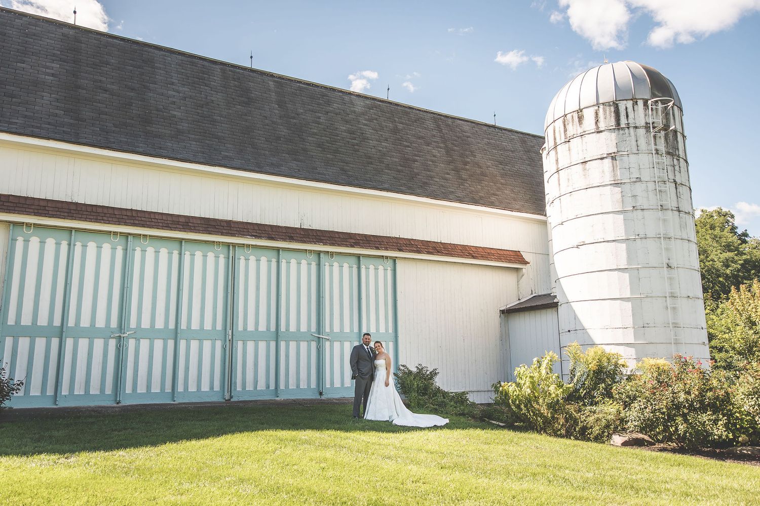 Wedding photos taken against white farm buildings with distinctive silos in the background.