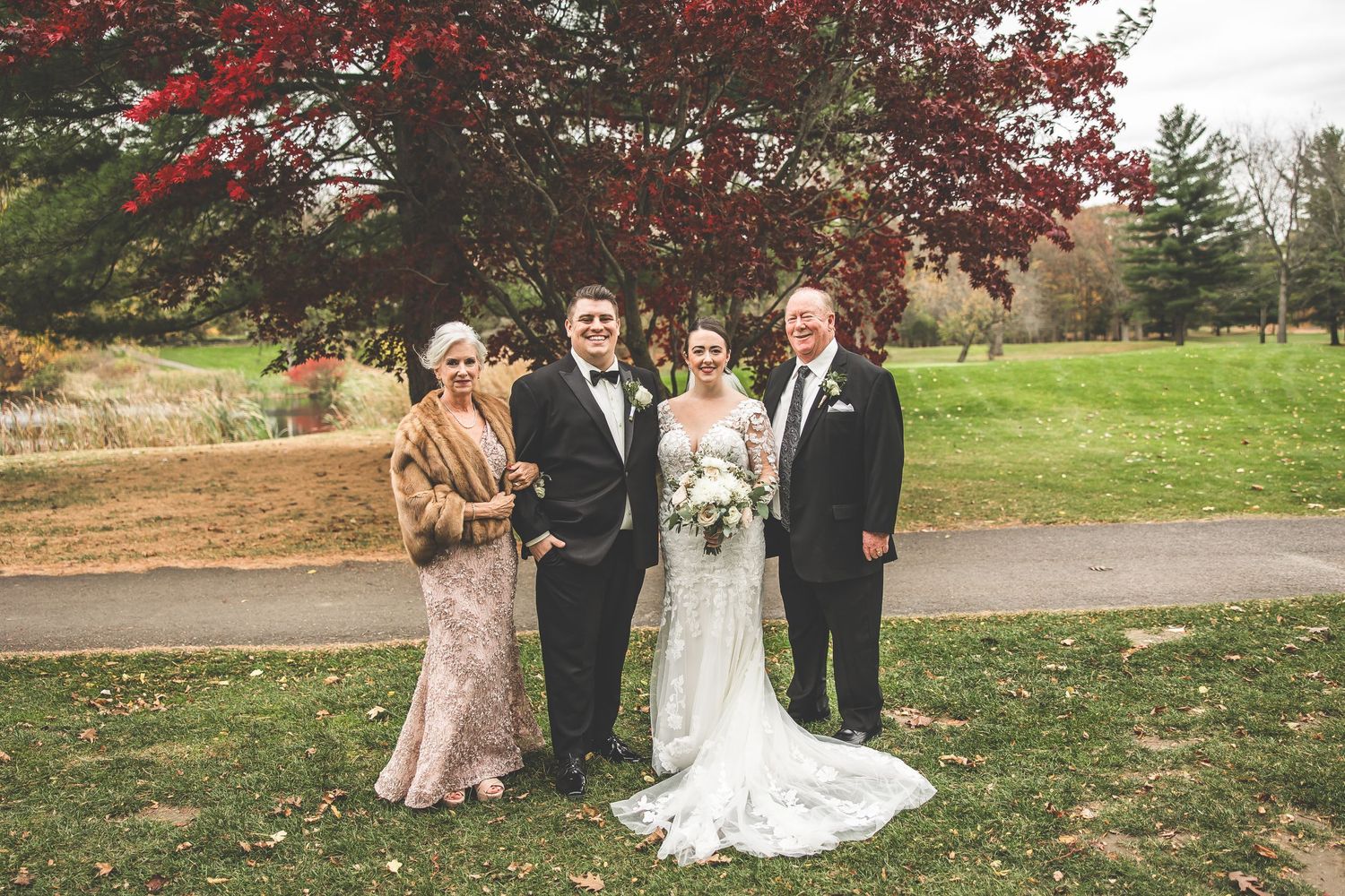 Wedding group photo session on lawn with autumn trees in background.