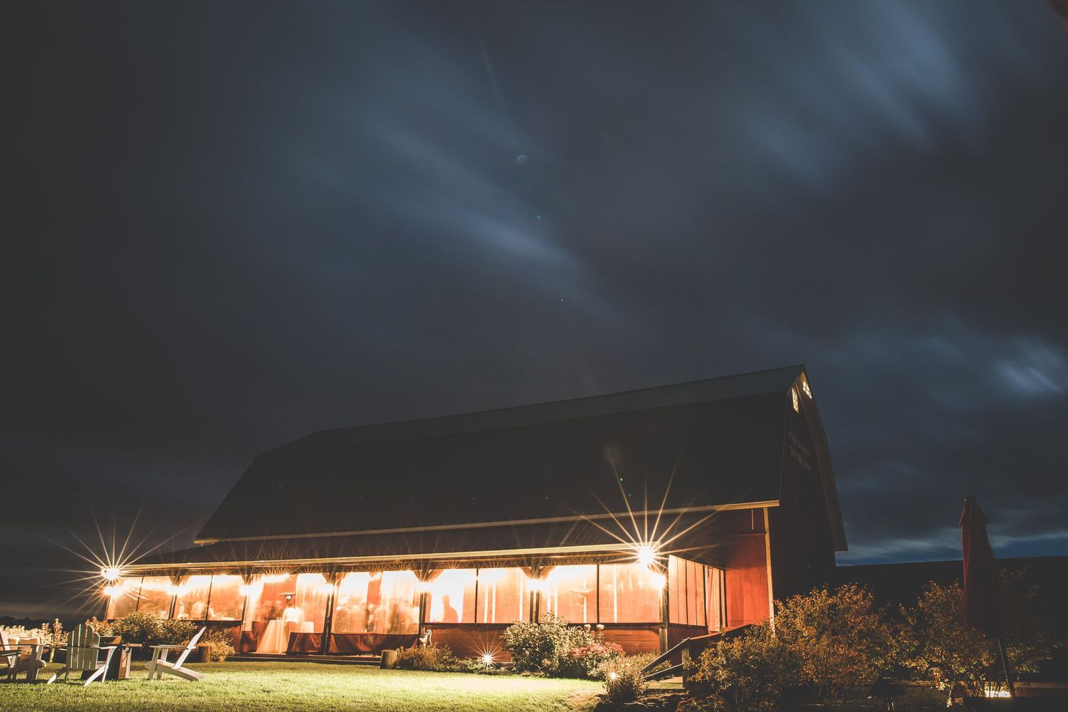 Panoramic nighttime view of an illuminated barn venue against a dramatic cloudy sky.