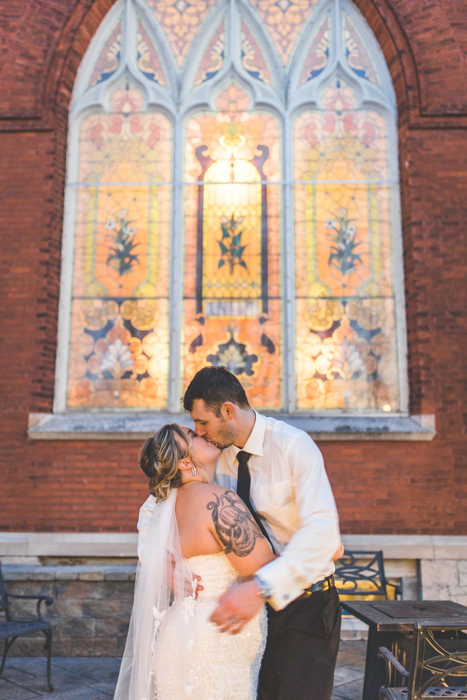 A couple shares an intimate moment in front of a beautiful illuminated church window at sunset.