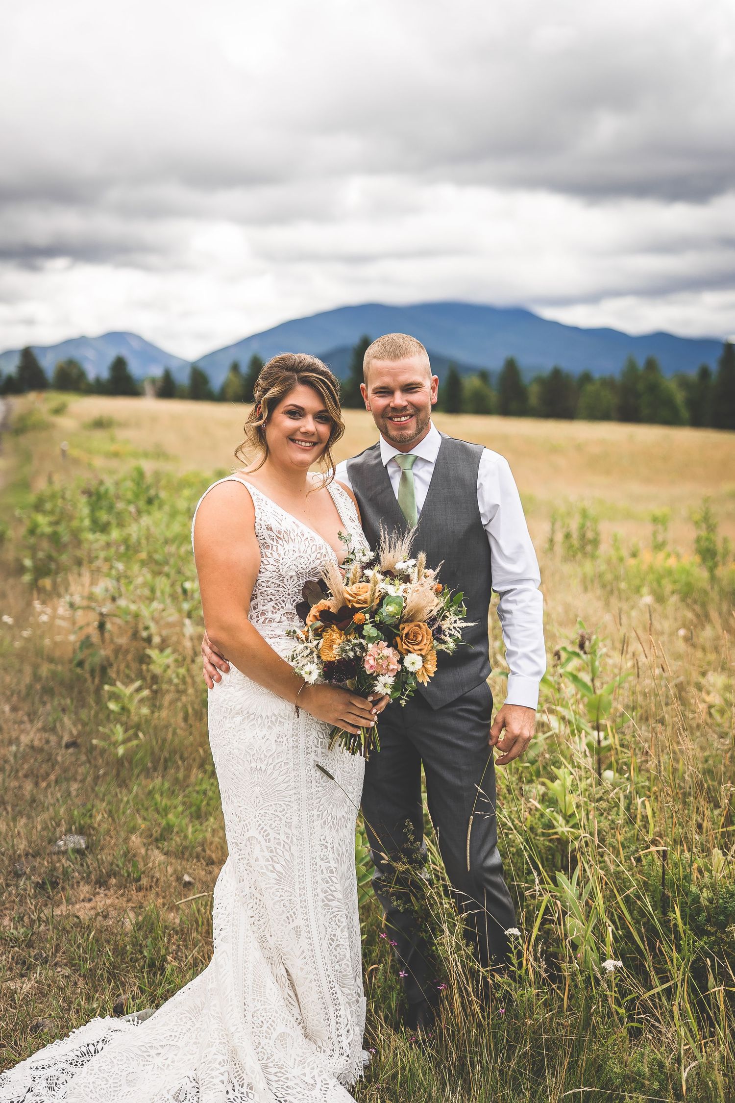 Wedding photography session in a scenic meadow with mountains and dramatic sky.