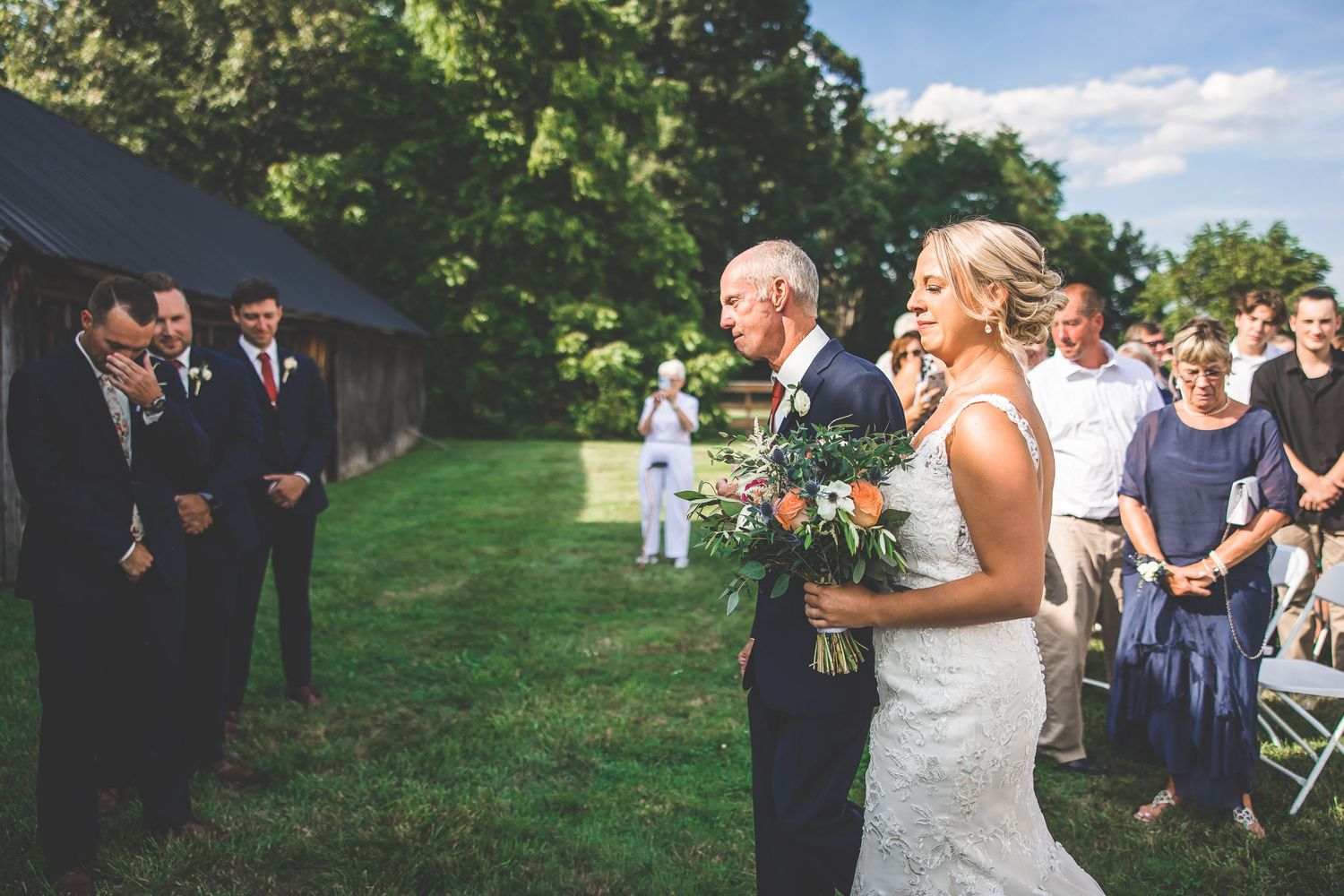 Outdoor wedding ceremony setup with wooden arch and white chairs against a bright blue summer sky.