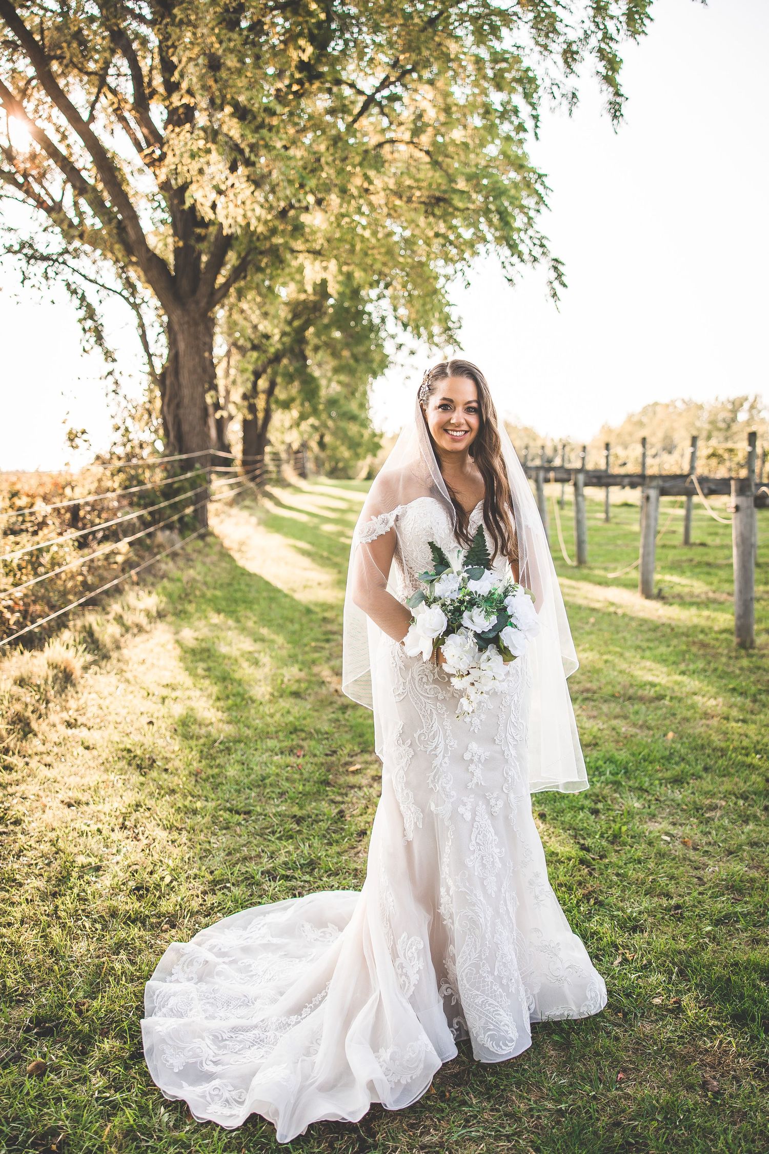 Bride in lace wedding gown poses gracefully on grassy hillside during golden hour.